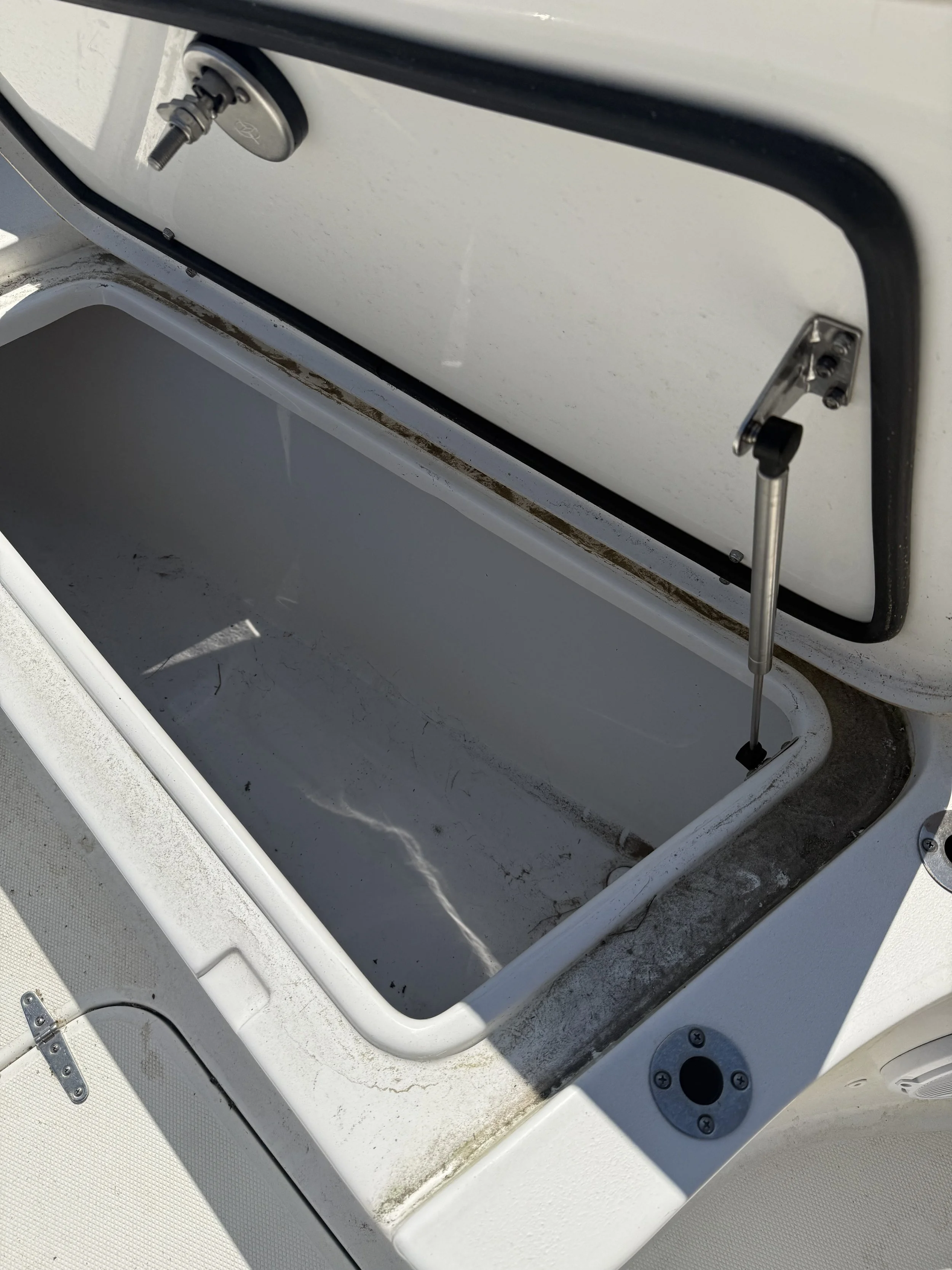 Open storage compartment on a white boat, showing dirt and rust inside