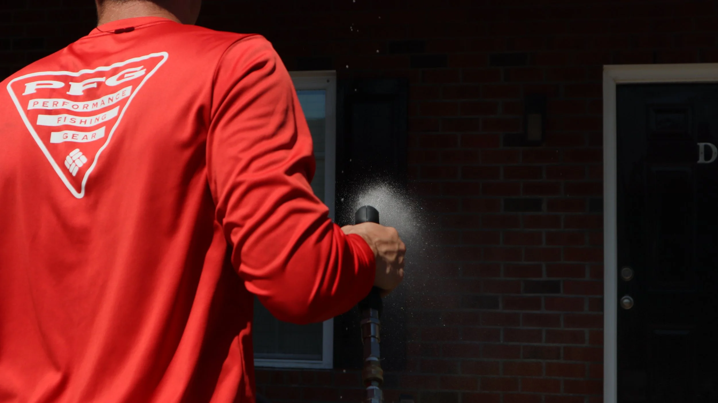 Person wearing a red jacket with a 'PFG Performance Fishing Gear' logo on the back, holding a pressure washer and spraying water.