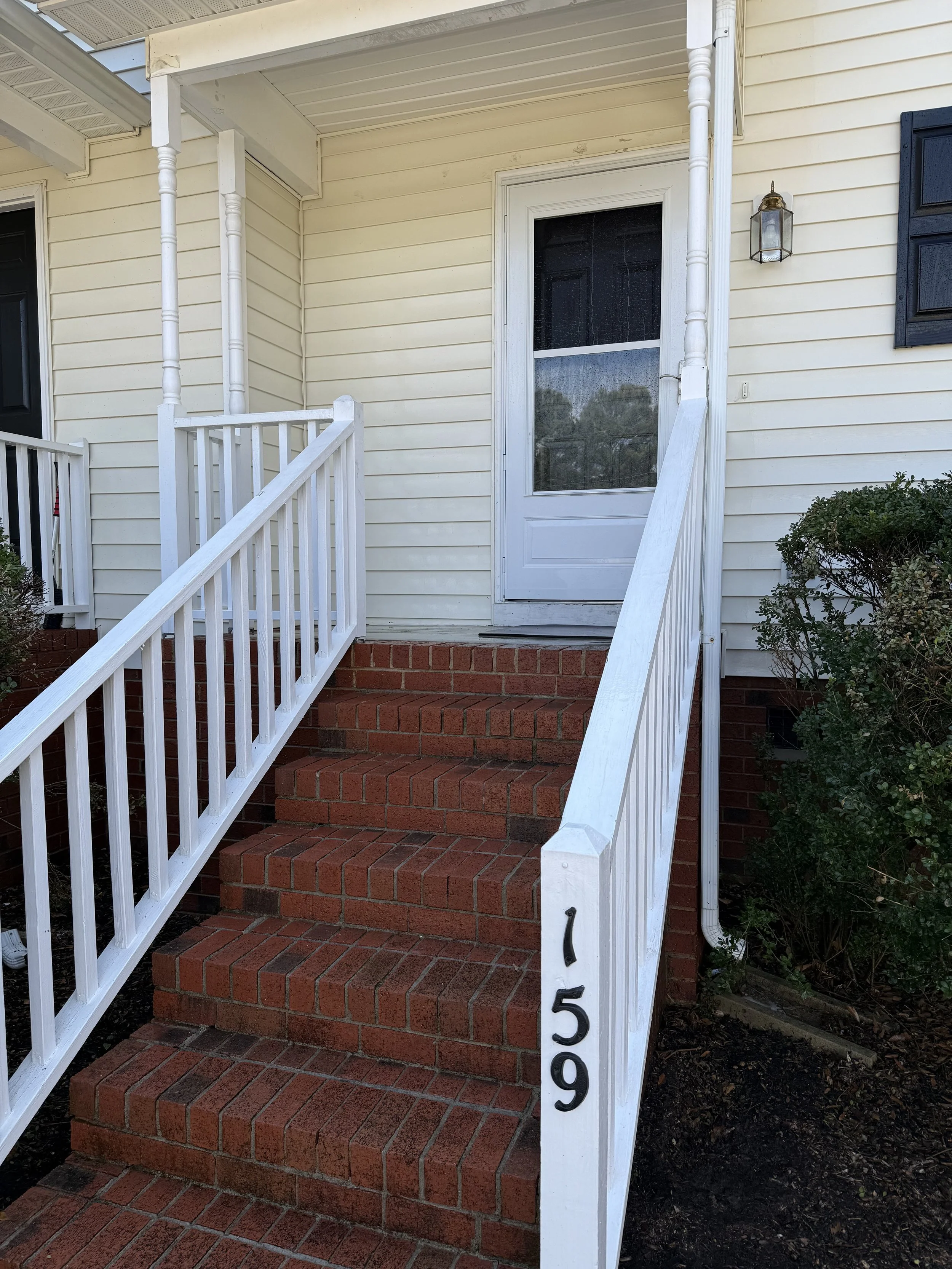 Front porch with brick stairs, white railing, and a screen door, house number 509, a small shrub on the right, and a wall-mounted outdoor lantern