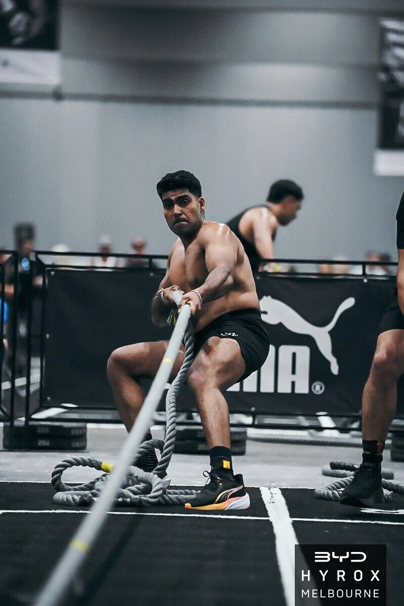 A shirtless man is participating in a rope pulling competition at BYD Hyrox Melbourne gym.