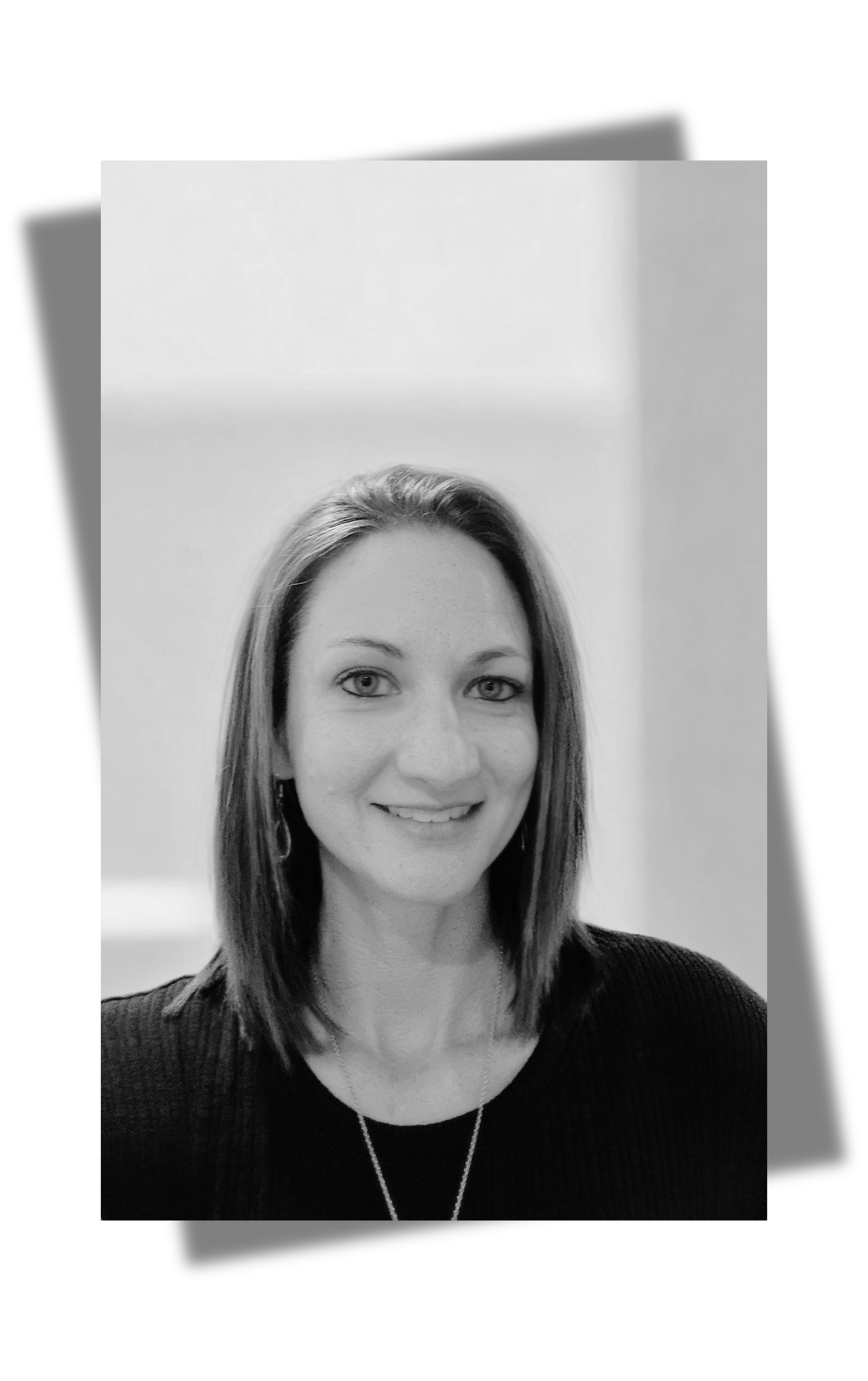 A black and white portrait of a woman with shoulder-length hair smiling at the camera, wearing a dark top and a necklace, with a plain background.