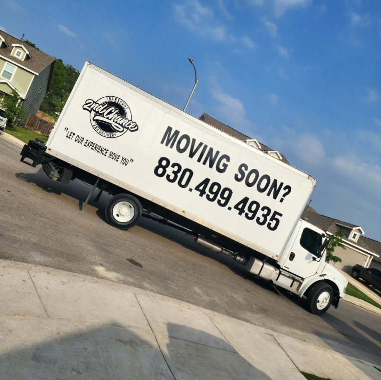 White moving truck parked on a residential street with a large sign on the side reading 'Moving Soon? 830.499.4935' and the logo '2nd Chance Transport & Delivery.'