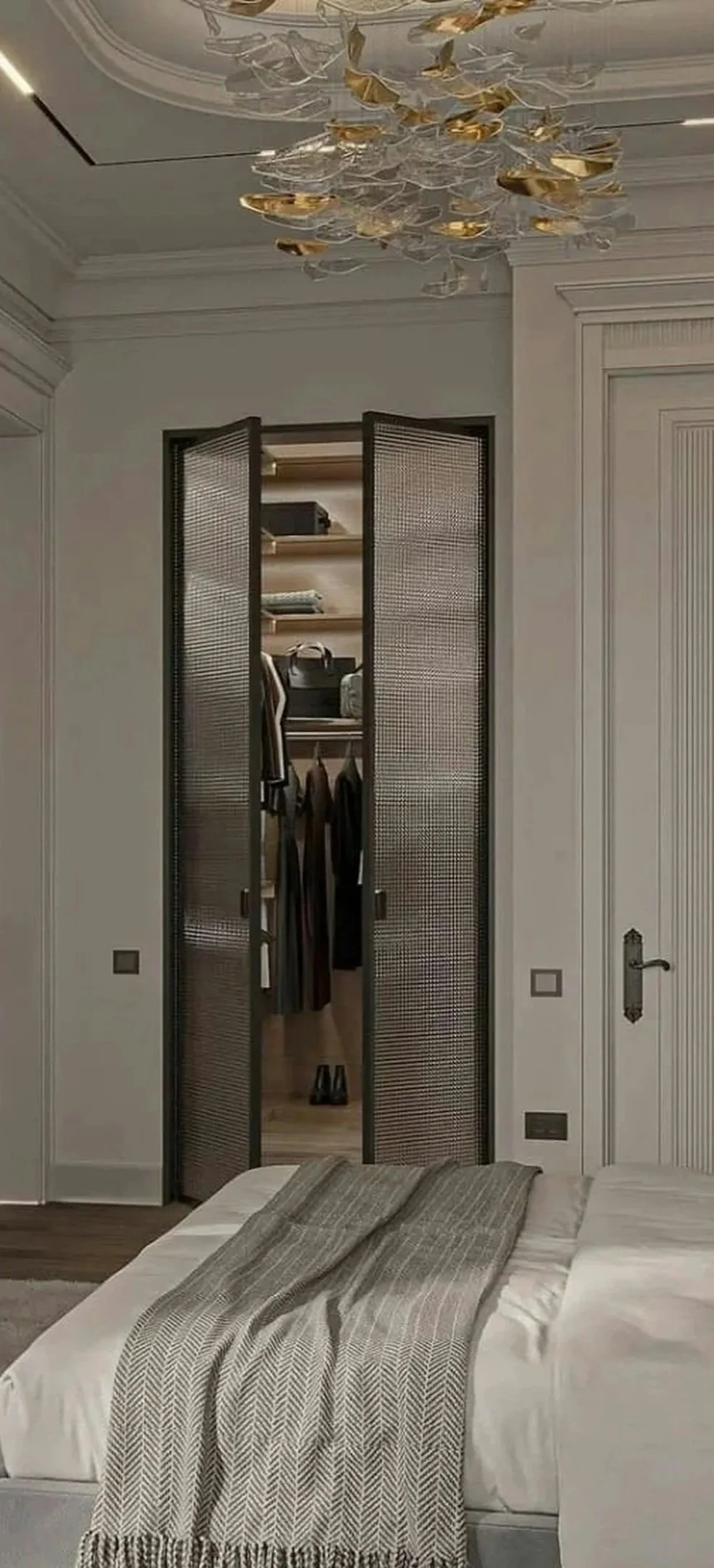 A bedroom with a bed and a closet with louvered doors open, showing clothes and shoes inside. There is a decorative chandelier hanging from the ceiling. West Hartford Closet Company WH Closet Co.