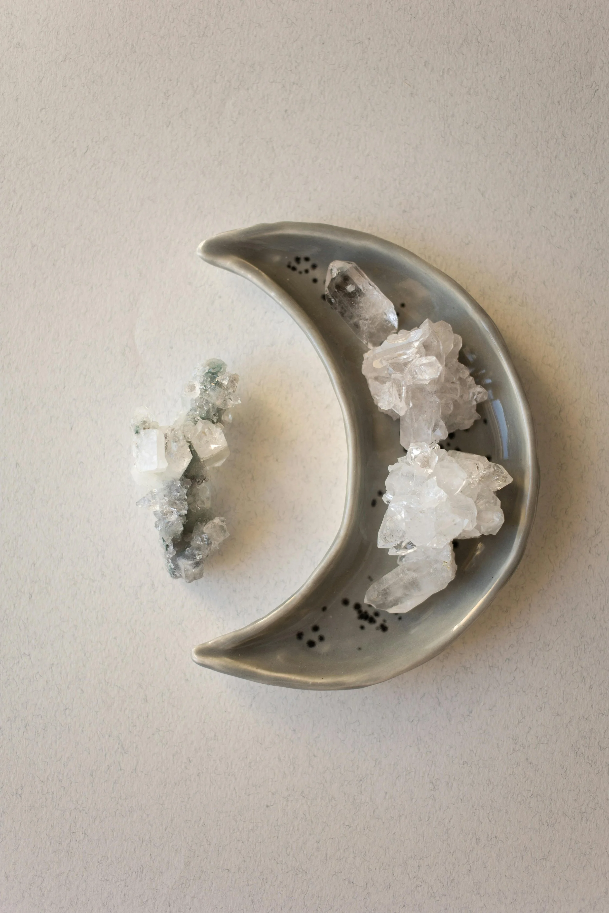 A crescent-shaped metal dish holding clear quartz crystals, with additional crystals placed on a white surface.