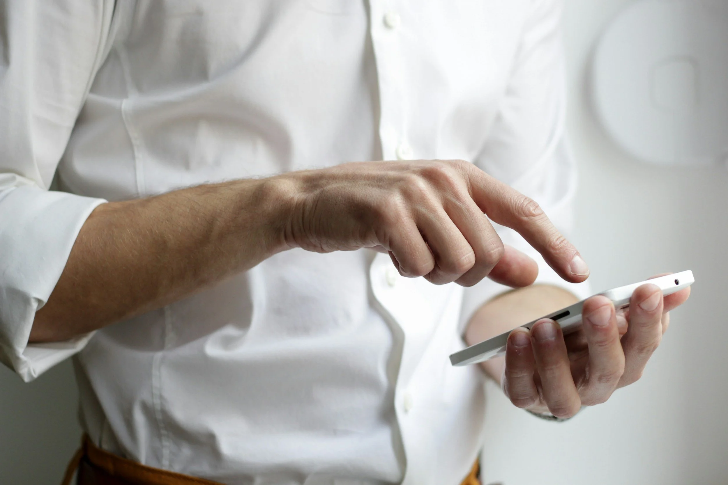 Person wearing a white button-down shirt holding and using a smartphone.