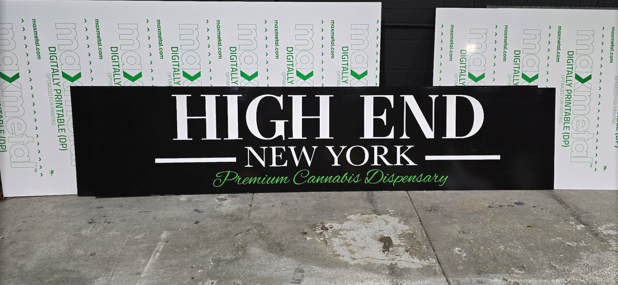 Sign for High End New York, a premium cannabis dispensary, placed on a concrete sidewalk with white and green printed protective material behind it.