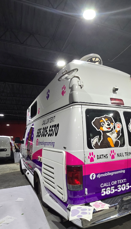 A mobile grooming van decorated with paw prints, a cartoon dog, and contact information for a grooming service.
