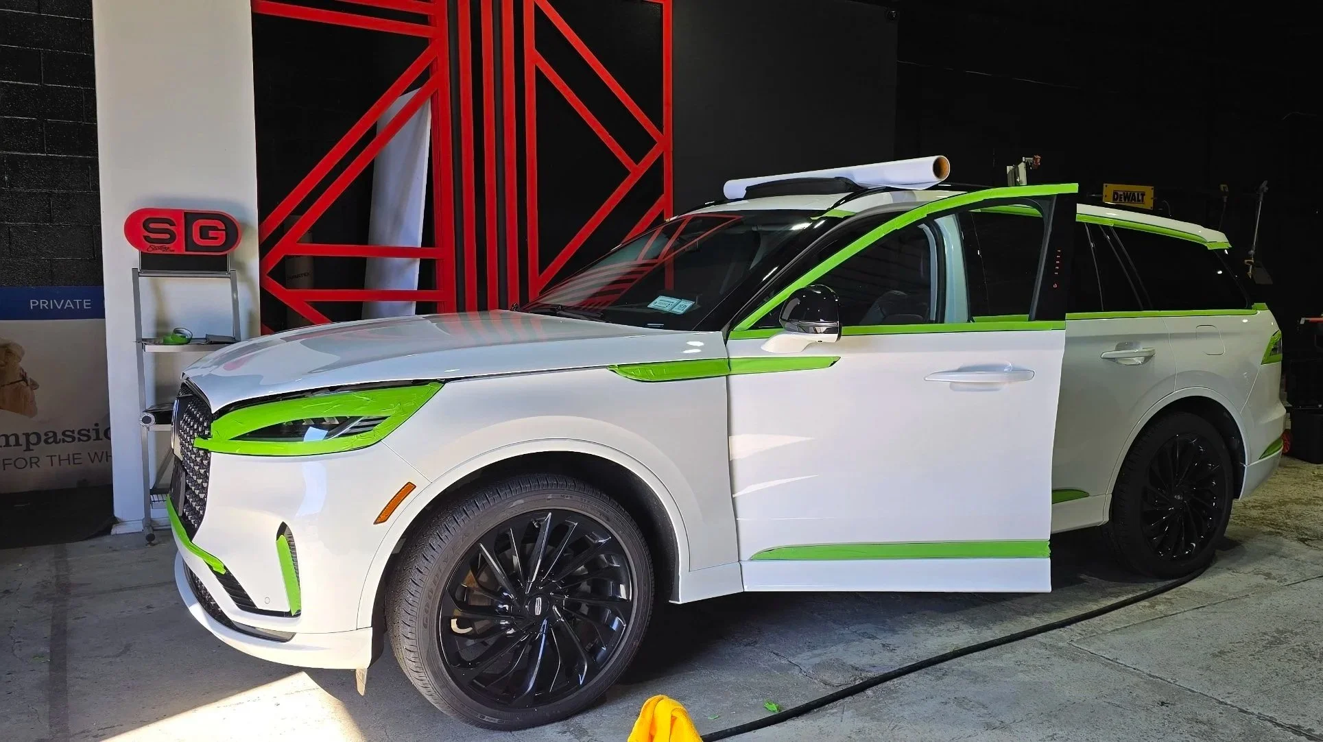 A white SUV with green accents parked indoors, with a roll of paper on its roof, near a red and black structure