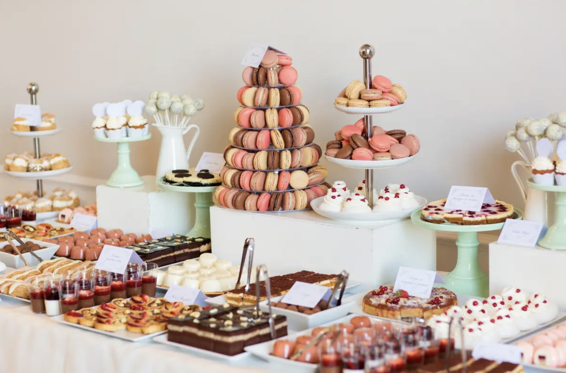 A dessert table with various pastries, macarons, cakes, and tarts displayed on tiered plates and trays at a celebration or event.