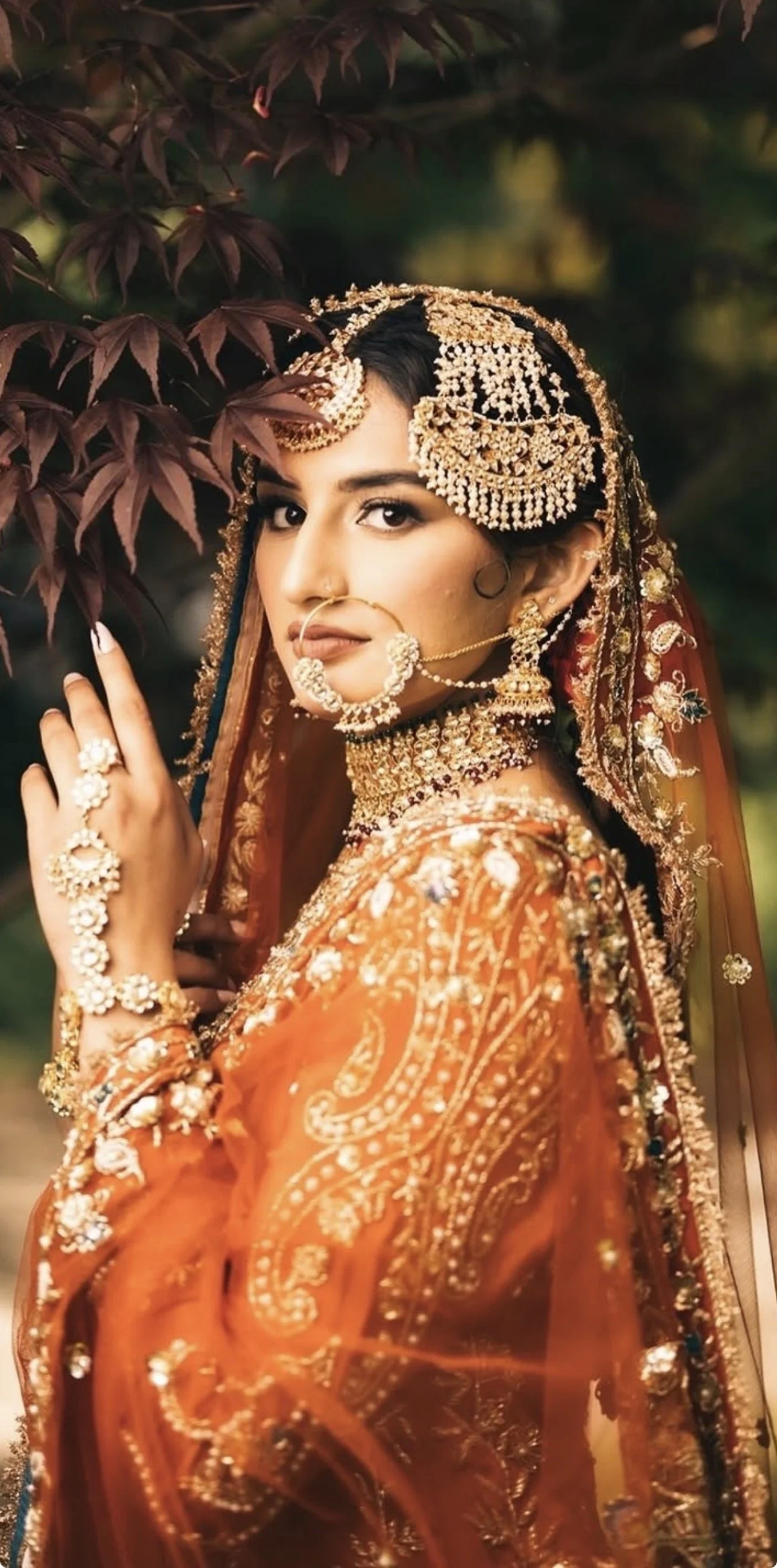 Indian bride in orange bridal outfit wearing polki and kundan jewelry set with nath and headpiece.