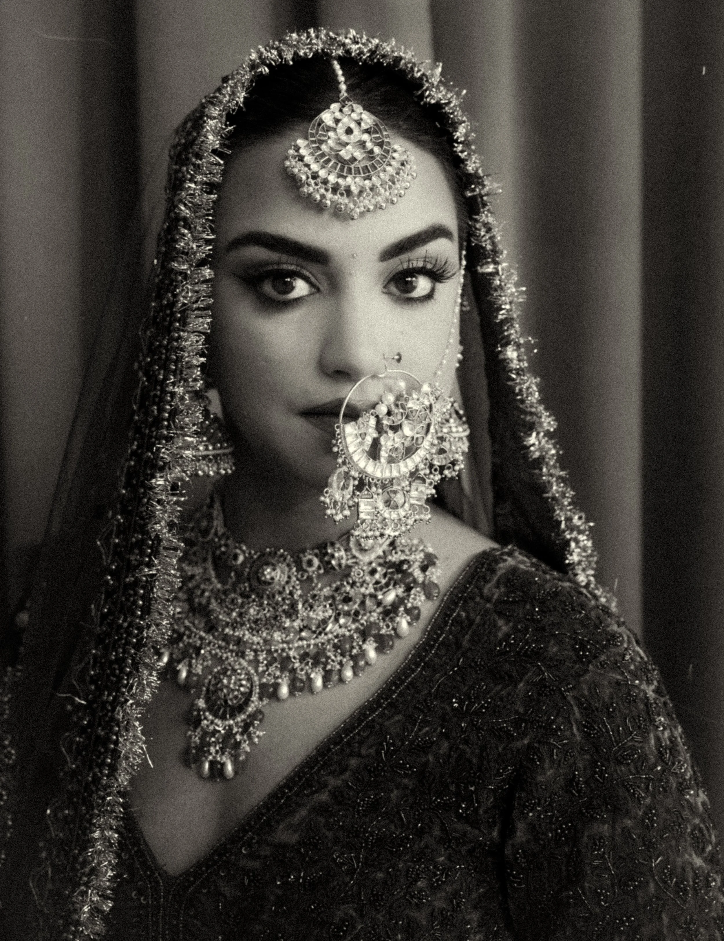 Black and white portrait of an Indian bride wearing kundan bridal jewelry including nath nose ring, maang tikka, and layered necklace styled for a traditional wedding look.