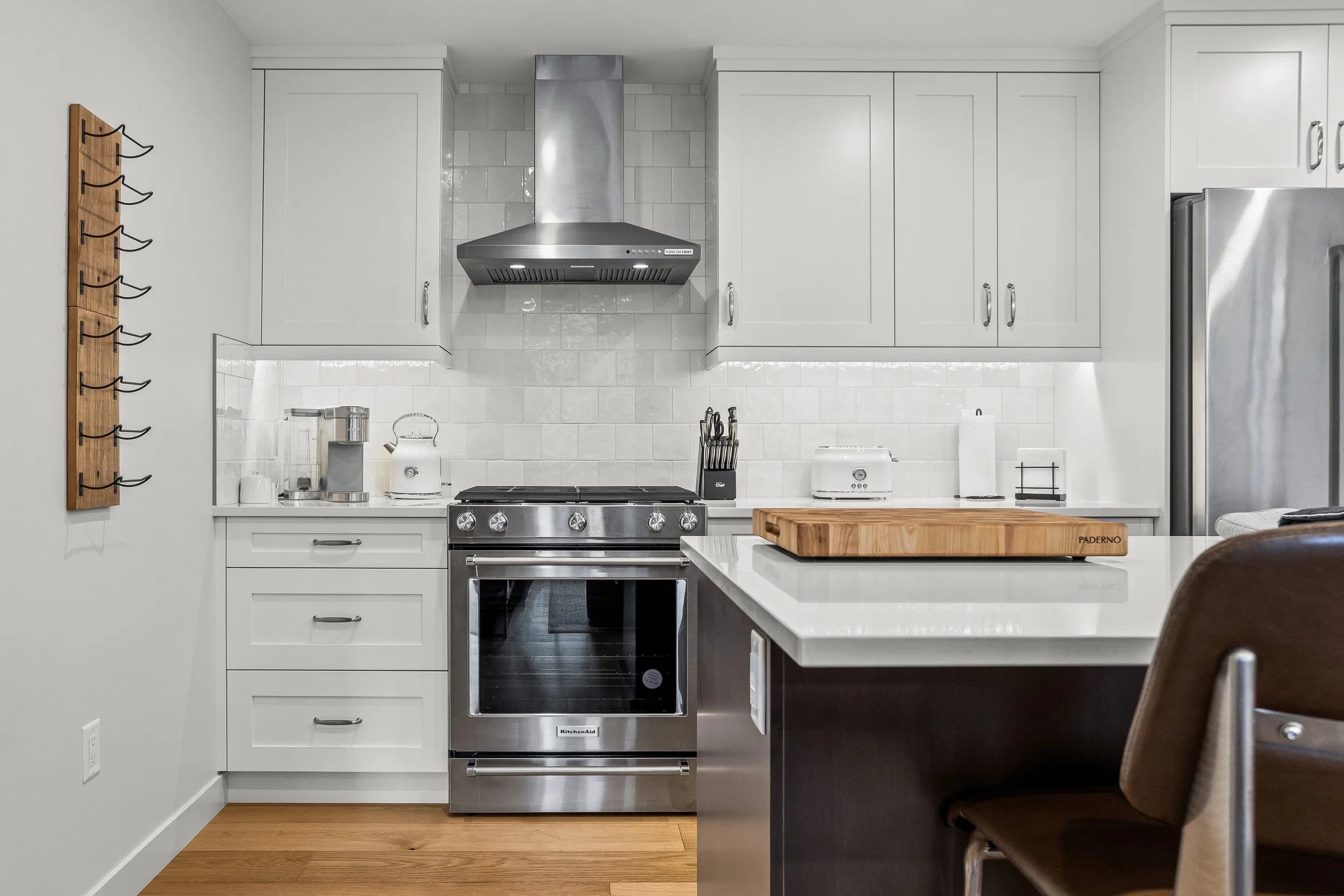 Modern kitchen with white cabinets, stainless steel appliances, including an oven and refrigerator, a wooden cutting board on the counter, and hardwood floors.