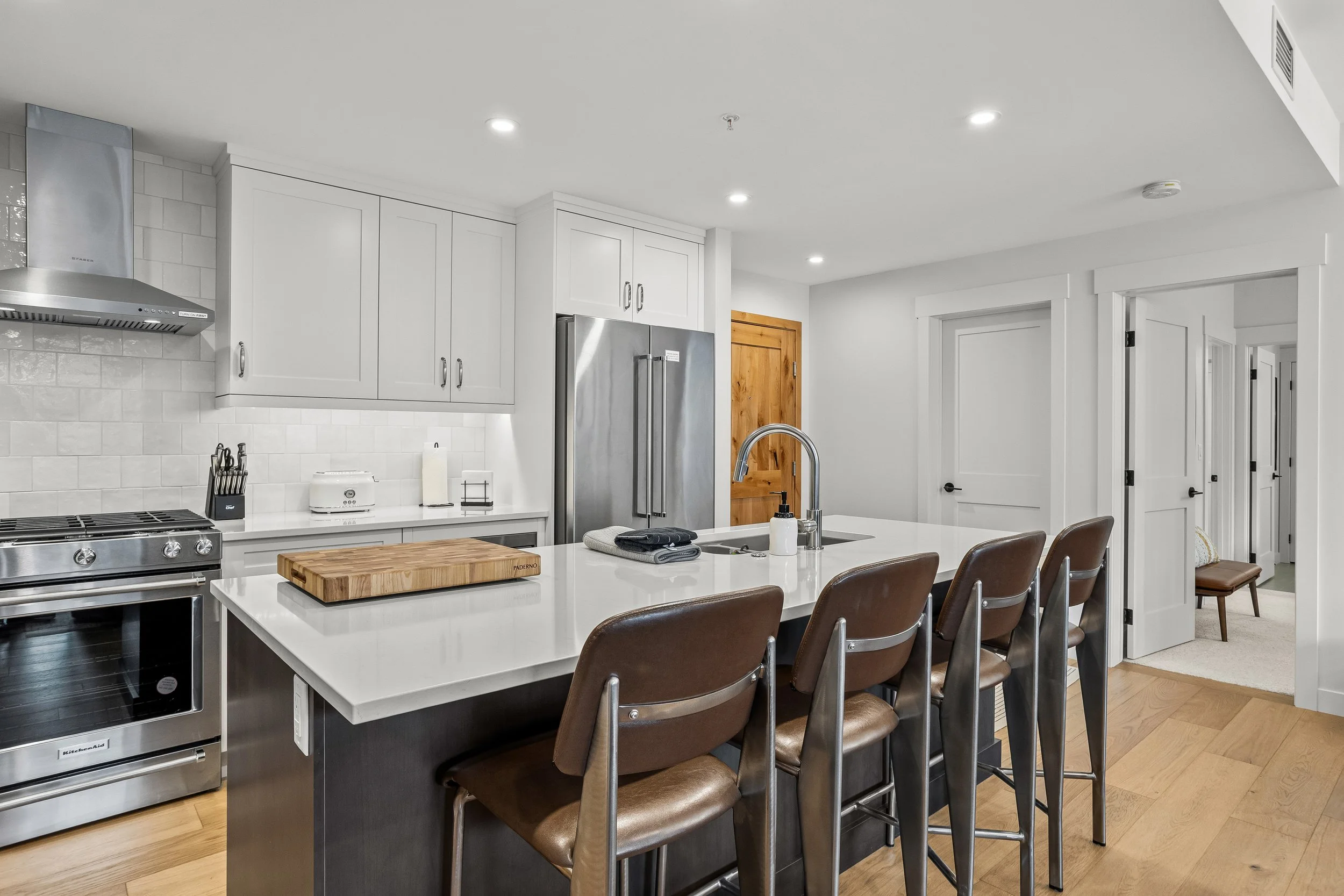 Modern kitchen with white cabinets, stainless steel appliances, a large island with bar stools, and wooden flooring.
