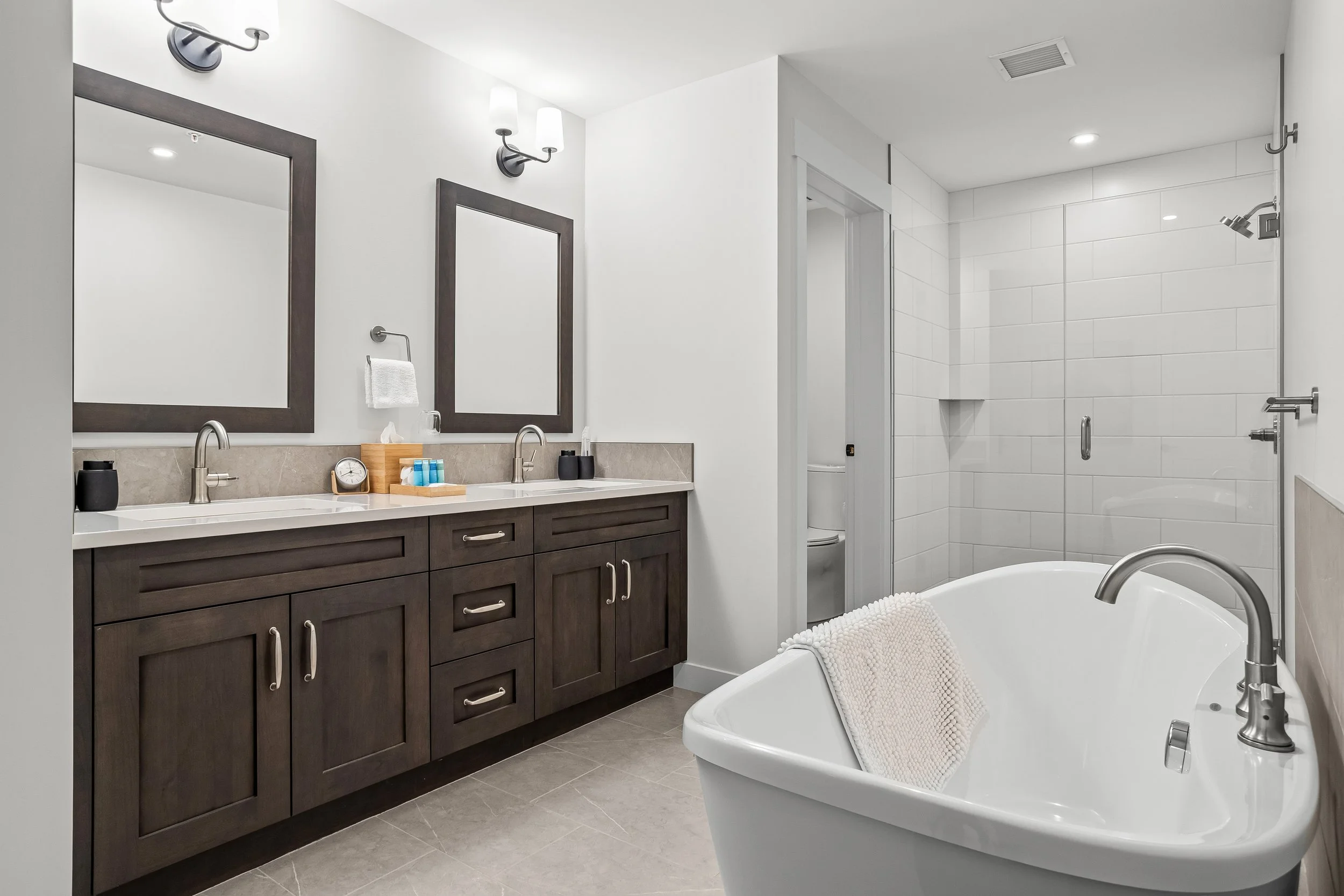 Modern bathroom with dual sinks, large mirrors, a bathtub with a towel, and a glass-enclosed walk-in shower.