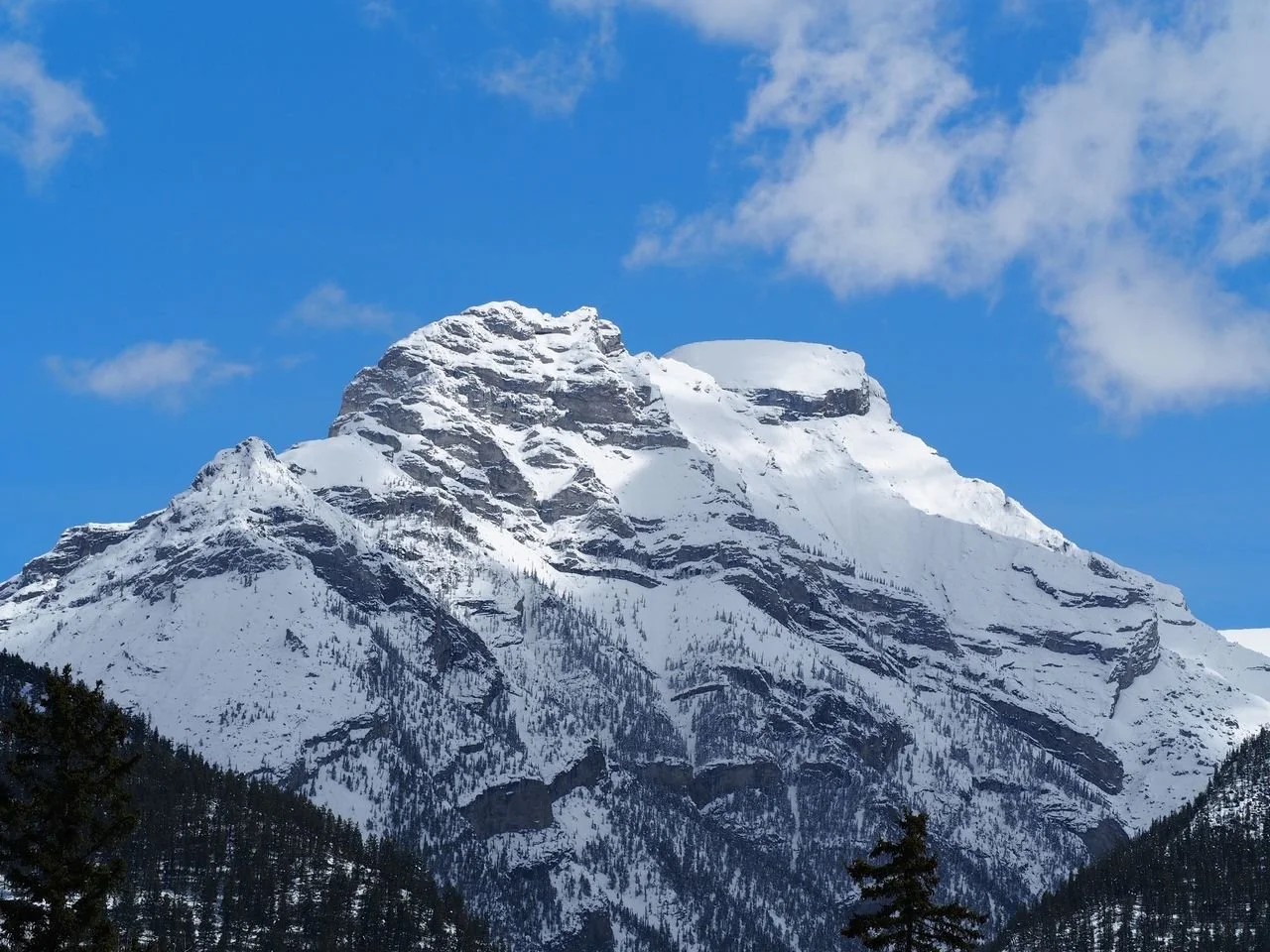 Snow-covered mountain peak with a bright blue sky and a few clouds in the background.