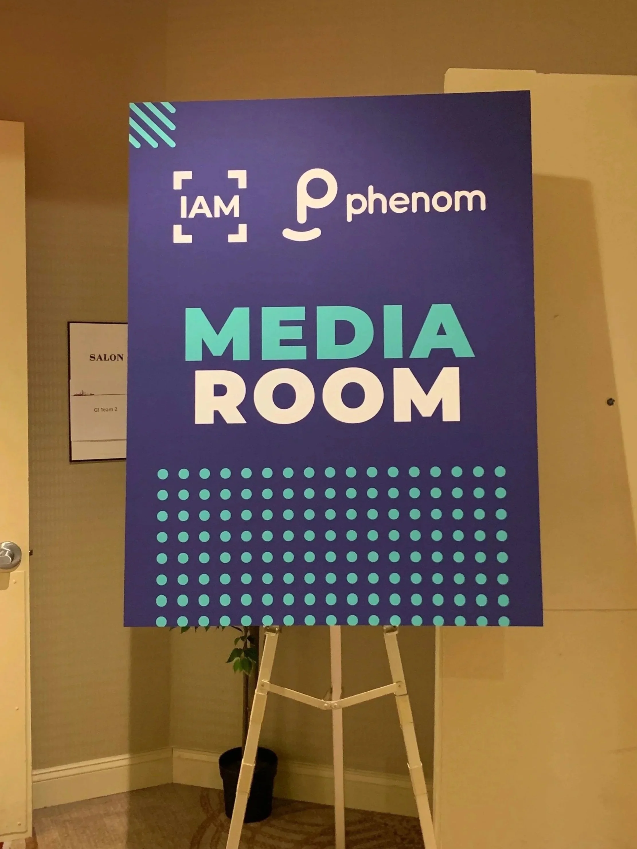 Sign indicating the media room for a user conference, featuring a purple background with teal and white text and design elements. Derek Herman, communications executive, hosted media interviews in this room at a user conference.