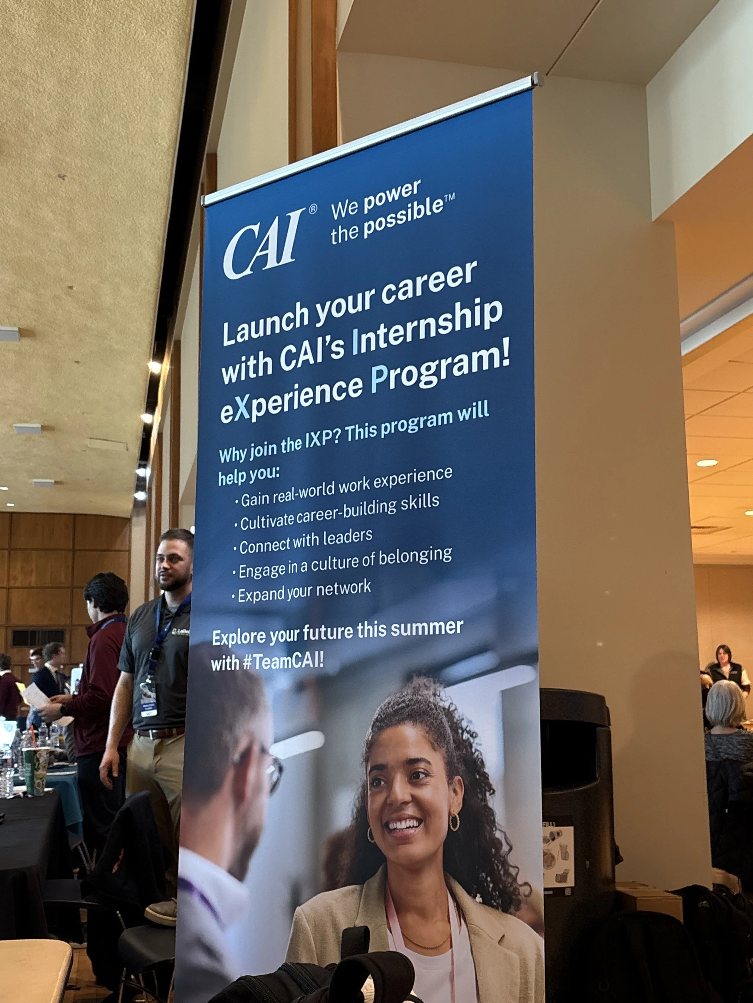Banner promoting a company's internship experience at a career event, with text detailing benefits like real-world work experience, career skills, and networking, with an image of a smiling woman and a man in a professional setting.