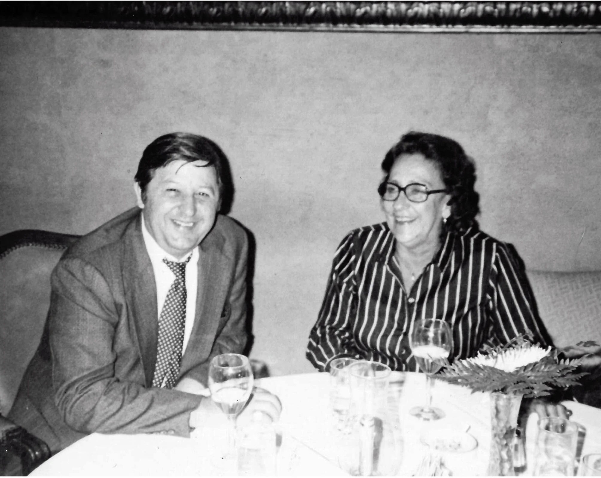 Jim and Helen Henry sitting at a table smiling, with a floral centerpiece in front of them.