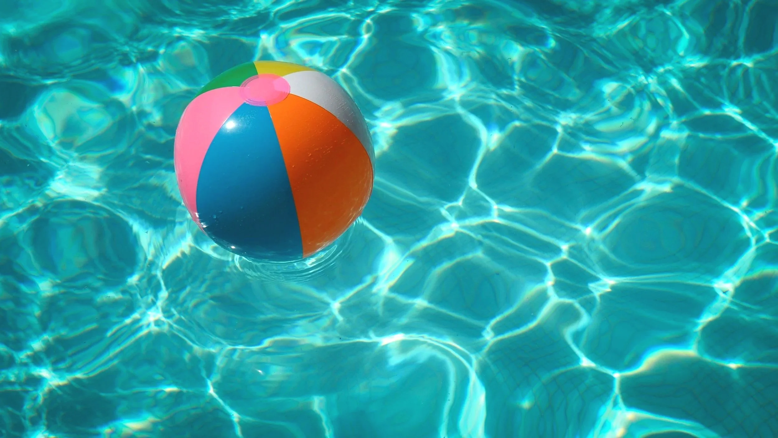 Colorful beach ball floating in a clean, blue swimming pool
