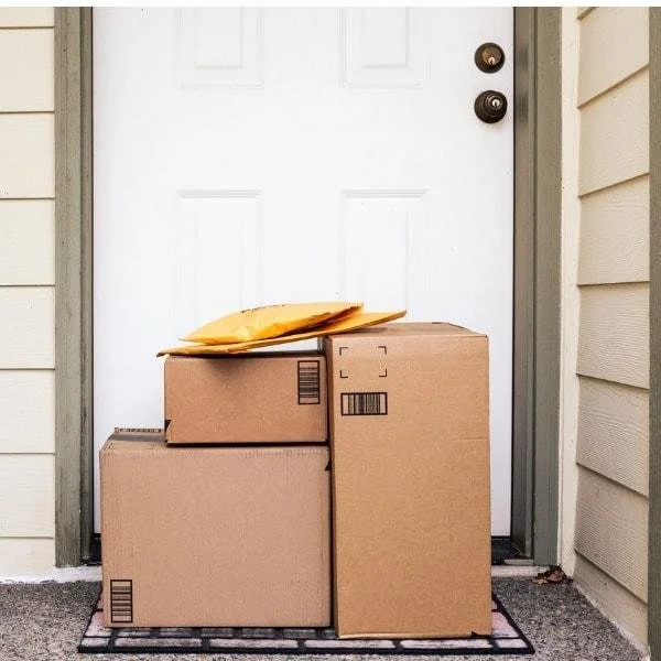 Trois cartons en carton empilés devant une porte blanche, avec un sac à enveloppe en papier posé dessus.