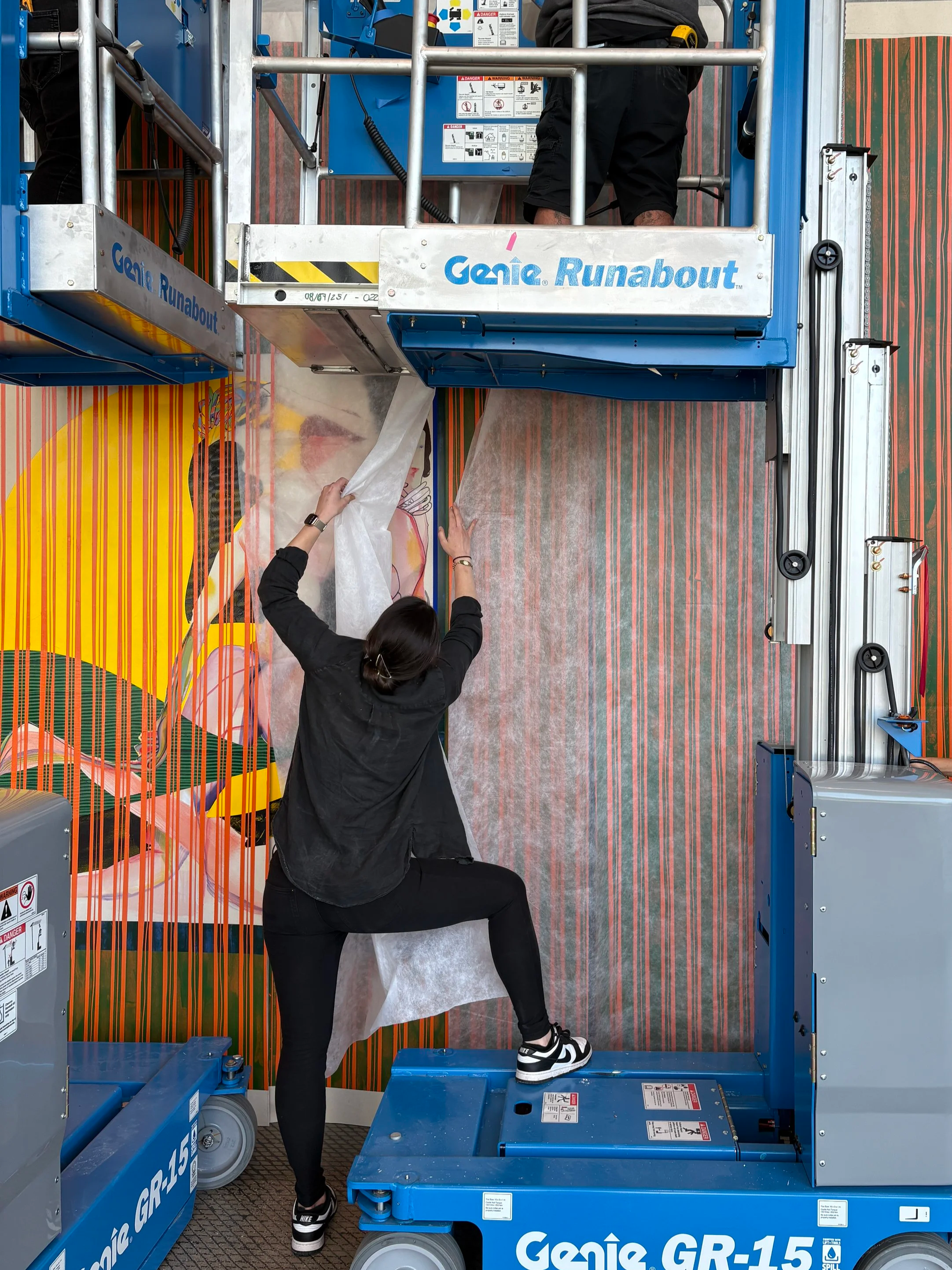 a woman is moving a piece of holitex to view a canvas as it is being installed.