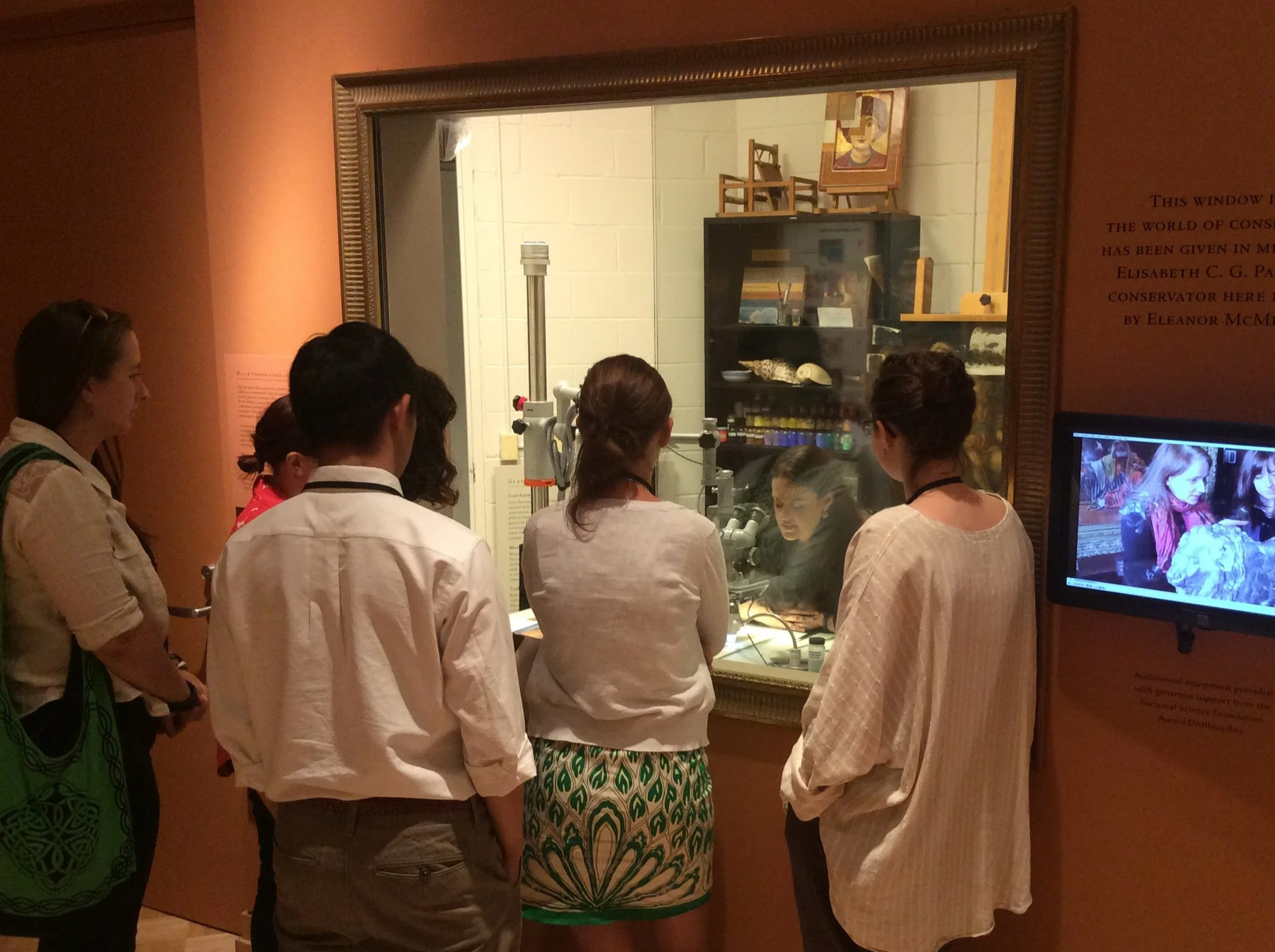Group of people standing in front of a glass display case at a museum, viewing art and artifacts.