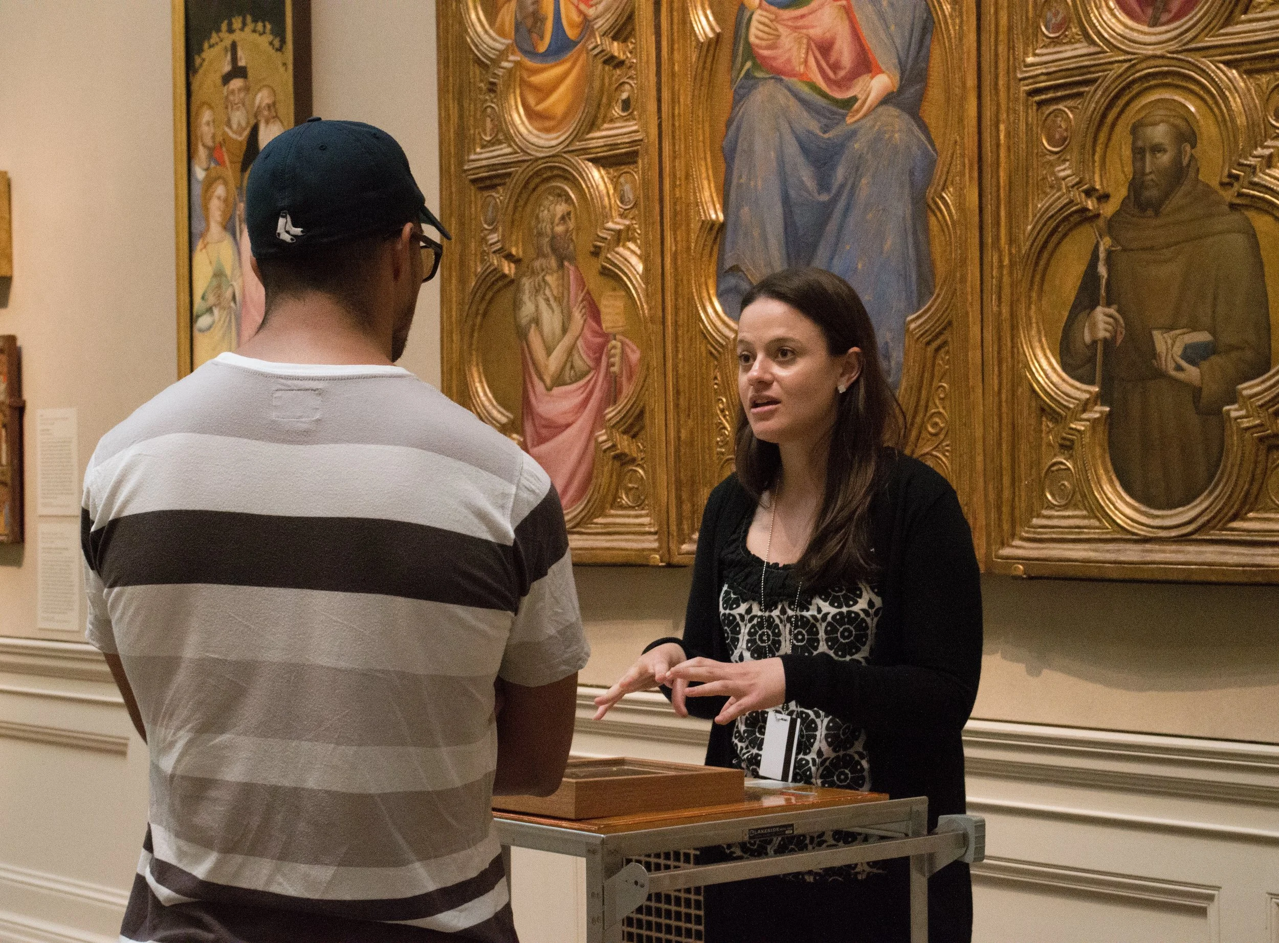 A woman converses with a man in front of religious paintings in an art museum or gallery.