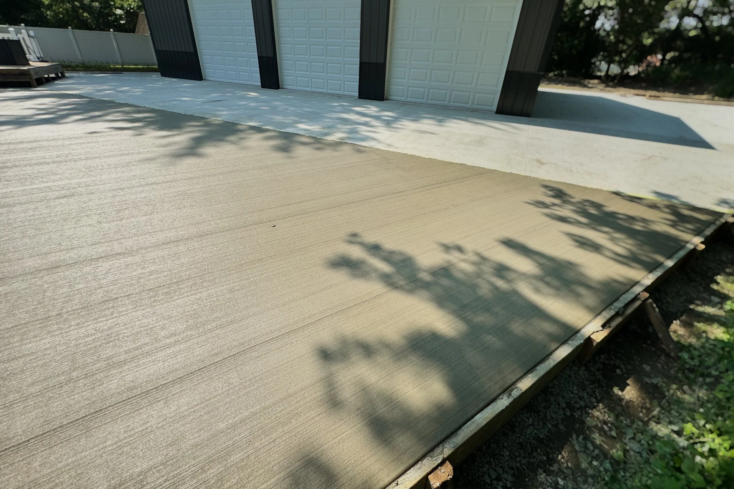 Side view of a garage with closed white door and black trim, concrete driveway, and shadows of trees on the ground.