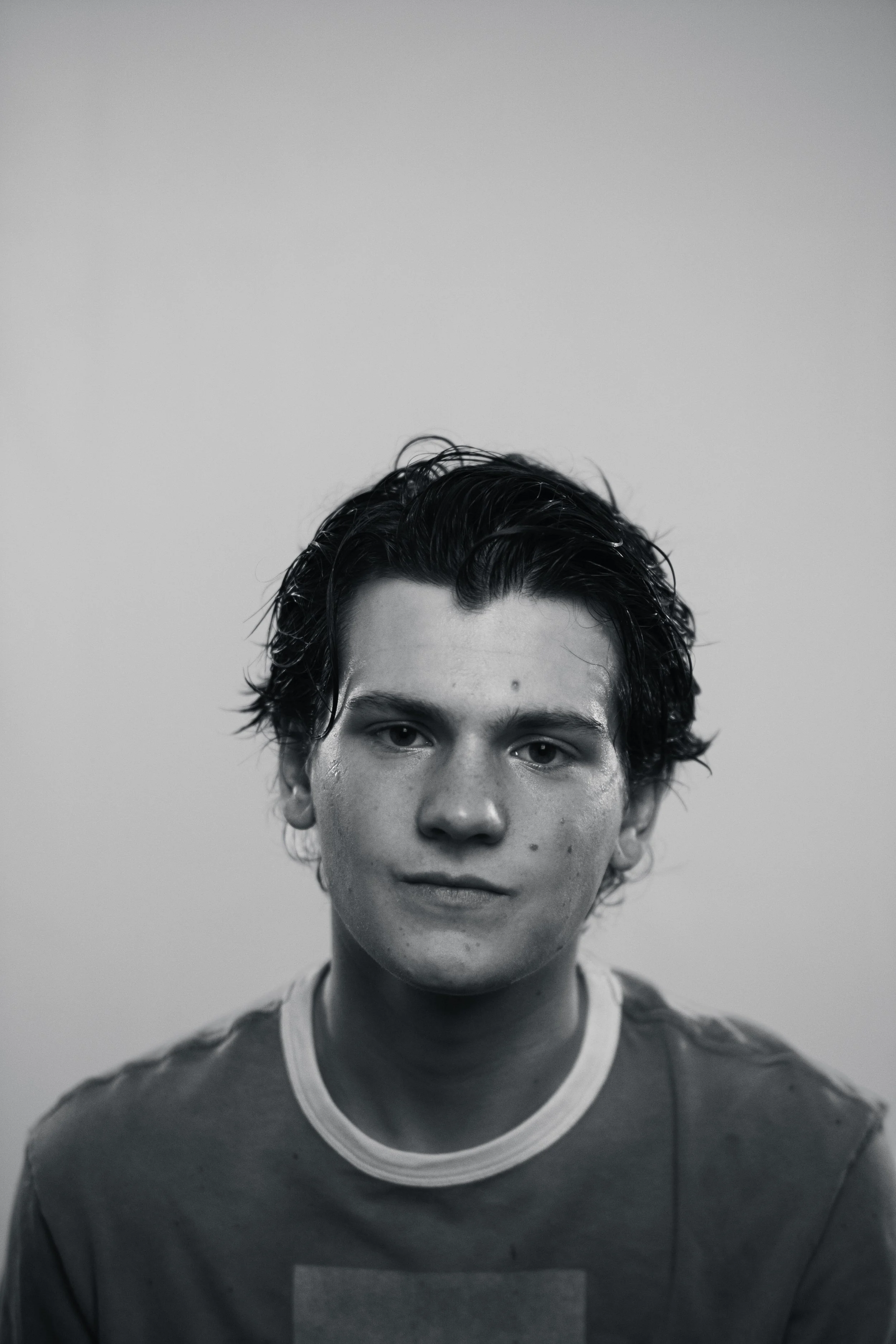 Black and white portrait of a young man with wet, dark hair, wearing a t-shirt with a rectangular graphic, against a plain background.
