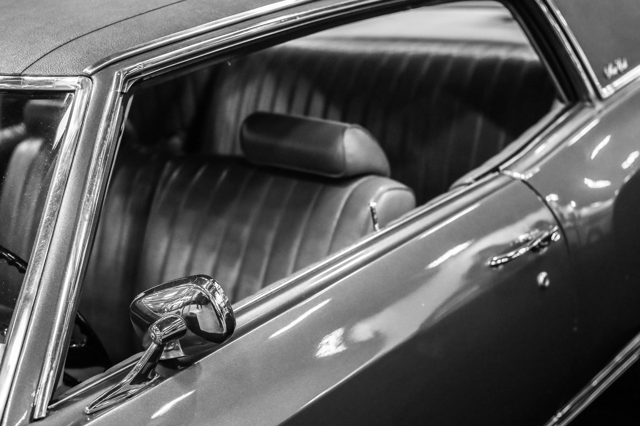 Close-up of a vintage convertible car's interior and exterior, featuring a leather seat, steering wheel, and side mirror.