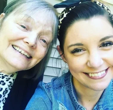 Two women smiling, close-up selfie, one with white hair and the other with dark hair wearing a headband.