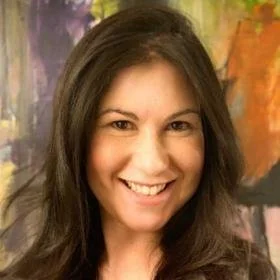 A woman with long brown hair smiling in front of a colorful abstract background.