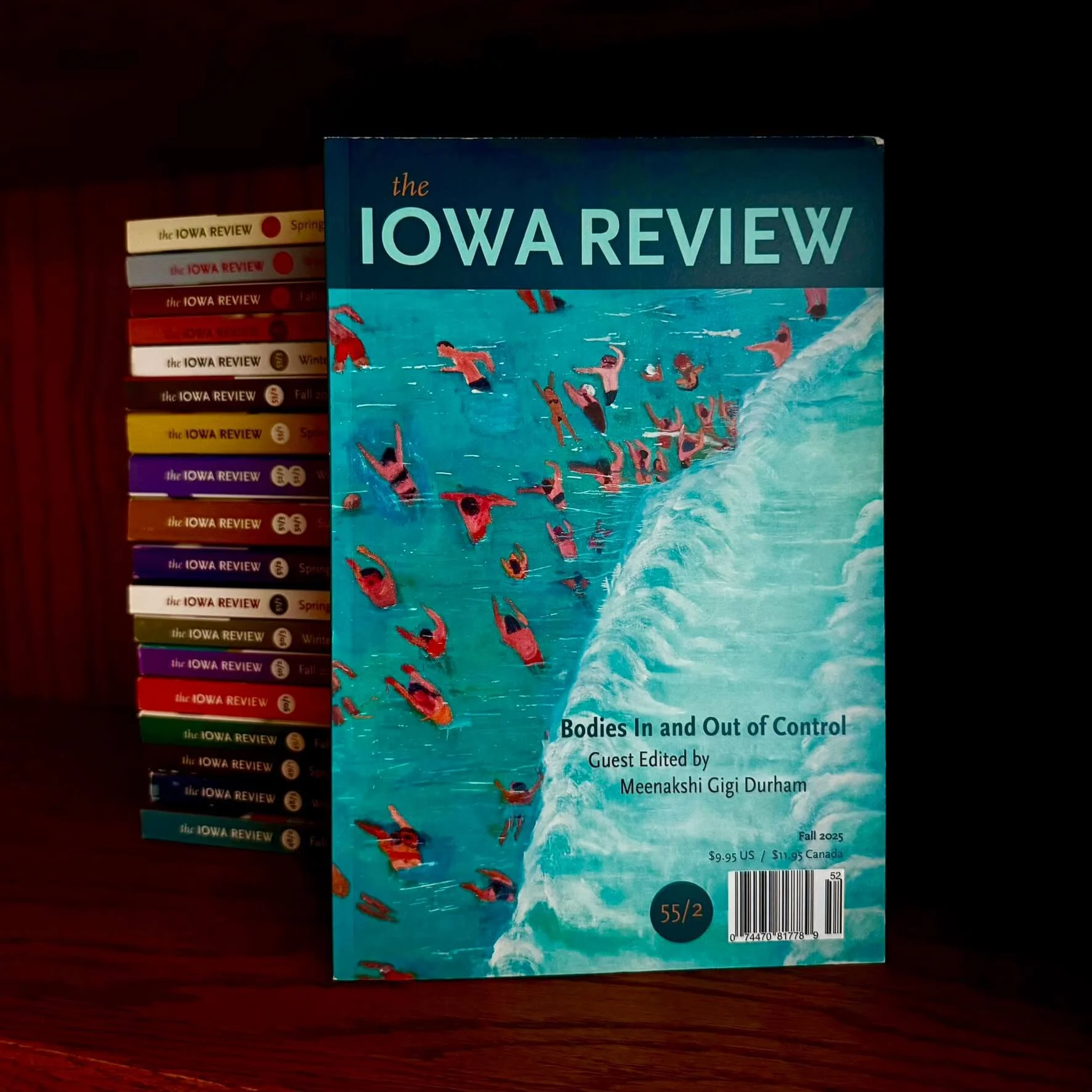 Cover of the Fall 2025 issue of The Iowa Review magazine, titled "Bodies In and Out of Control," next to a stack of back issues of The Iowa Review.