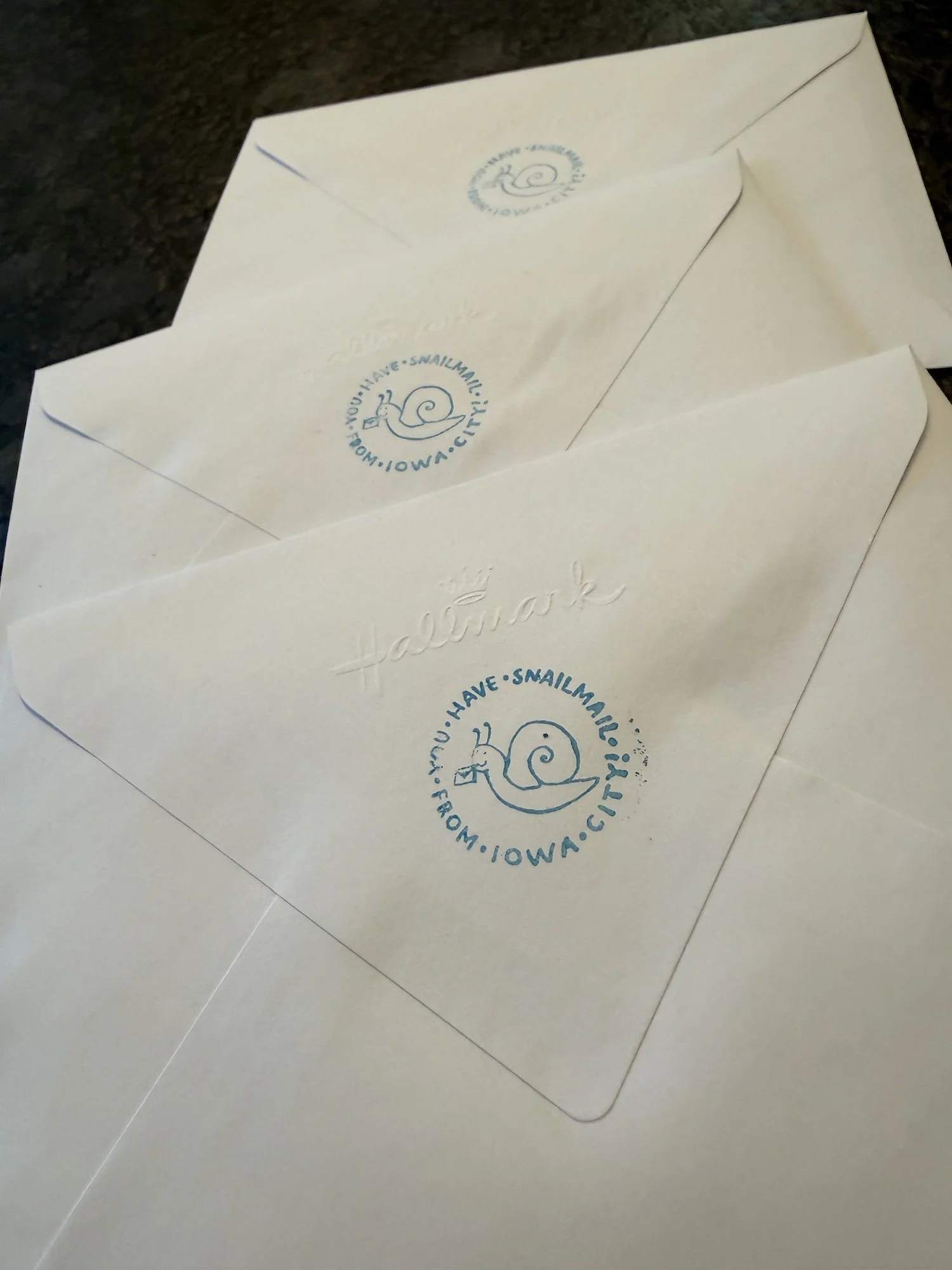 Three white envelopes stamped with a blue snail logo and the text 'You have snail mail from Iowa City"