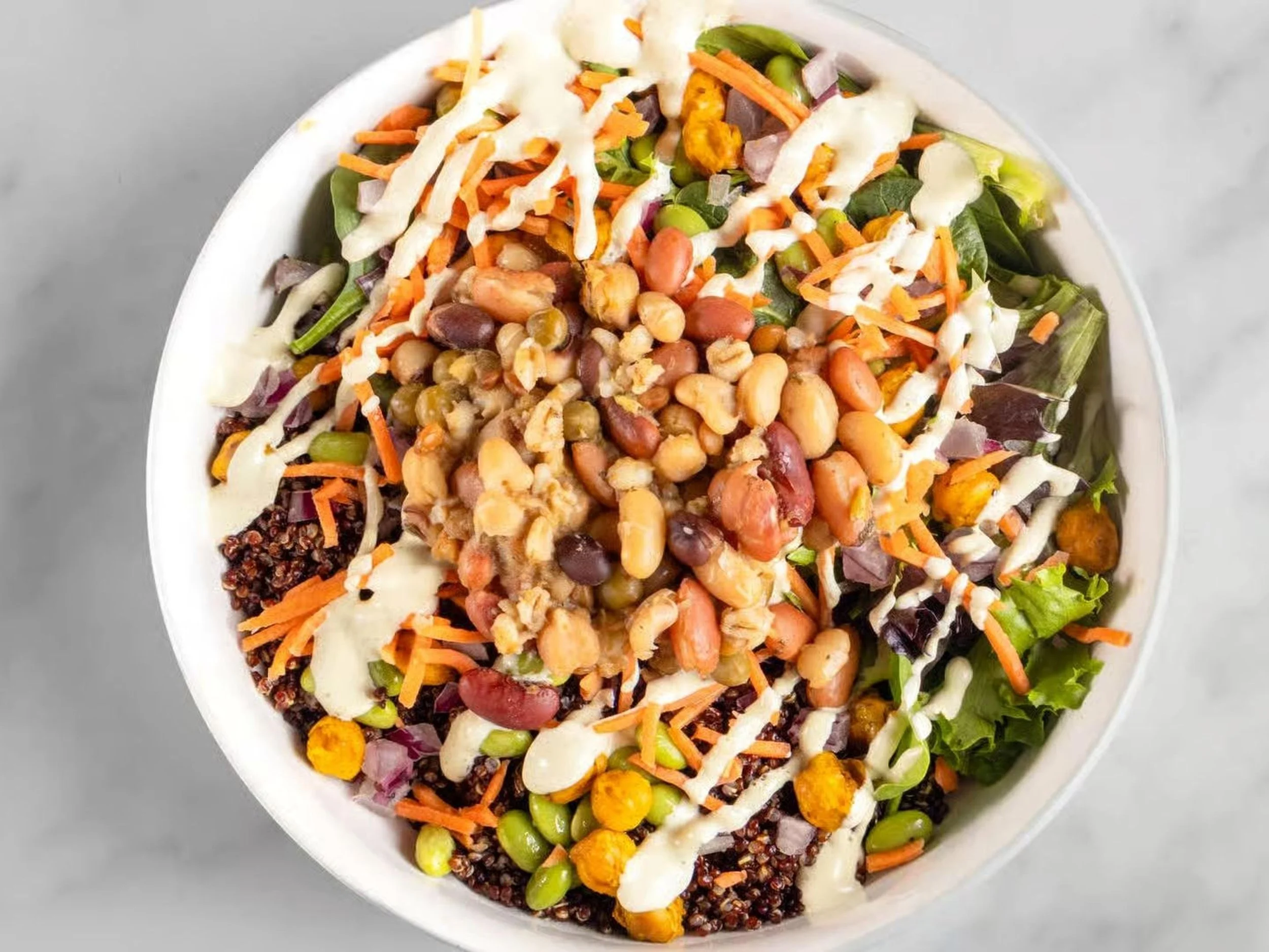 Bowl of mixed salad topped with beans and shredded vegetables, drizzled with a creamy dressing.