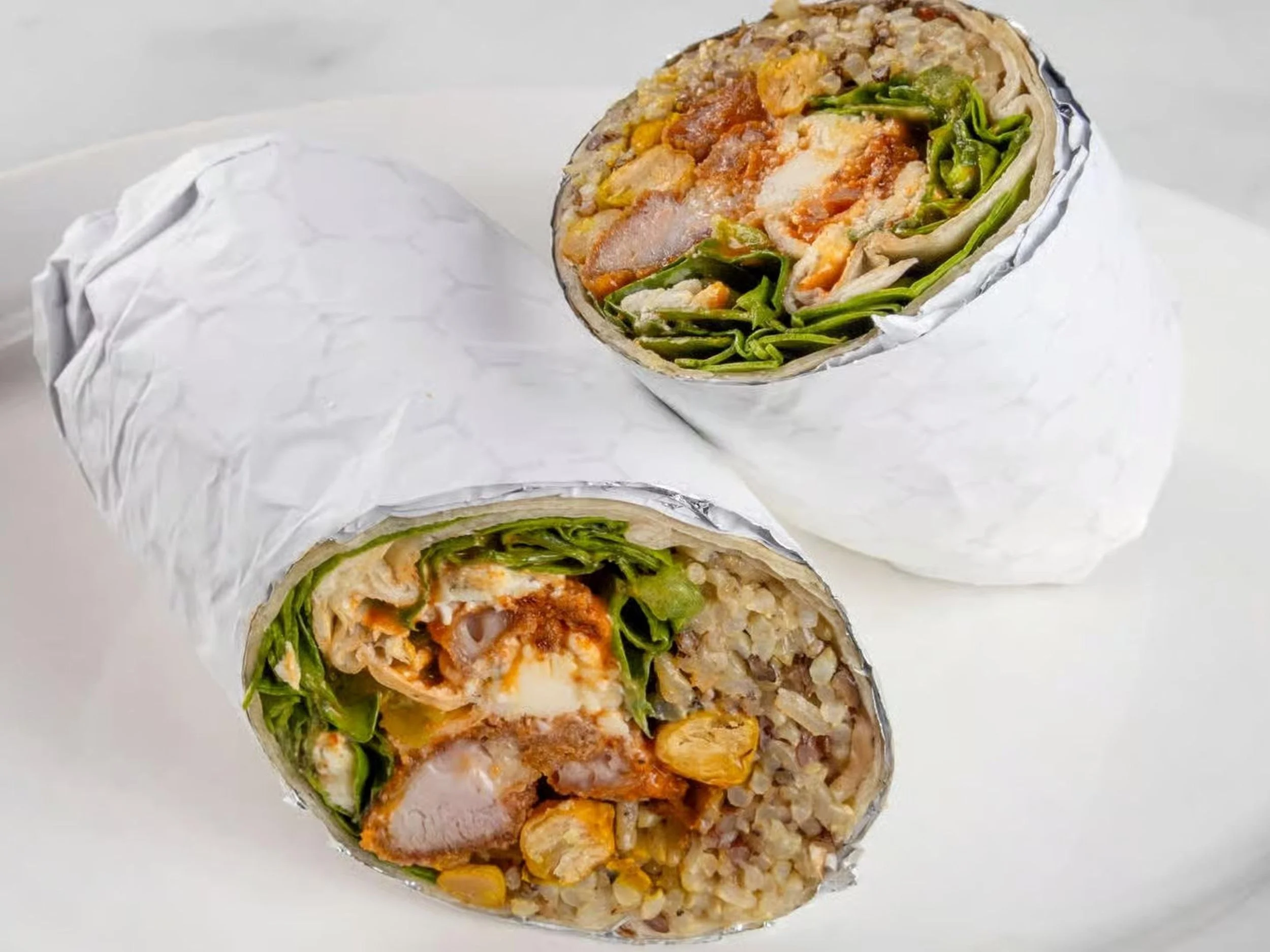 Close-up of a chicken burrito cut in half, showing rice, chicken, lettuce, corn, and sauce inside a wrapped flour tortilla.