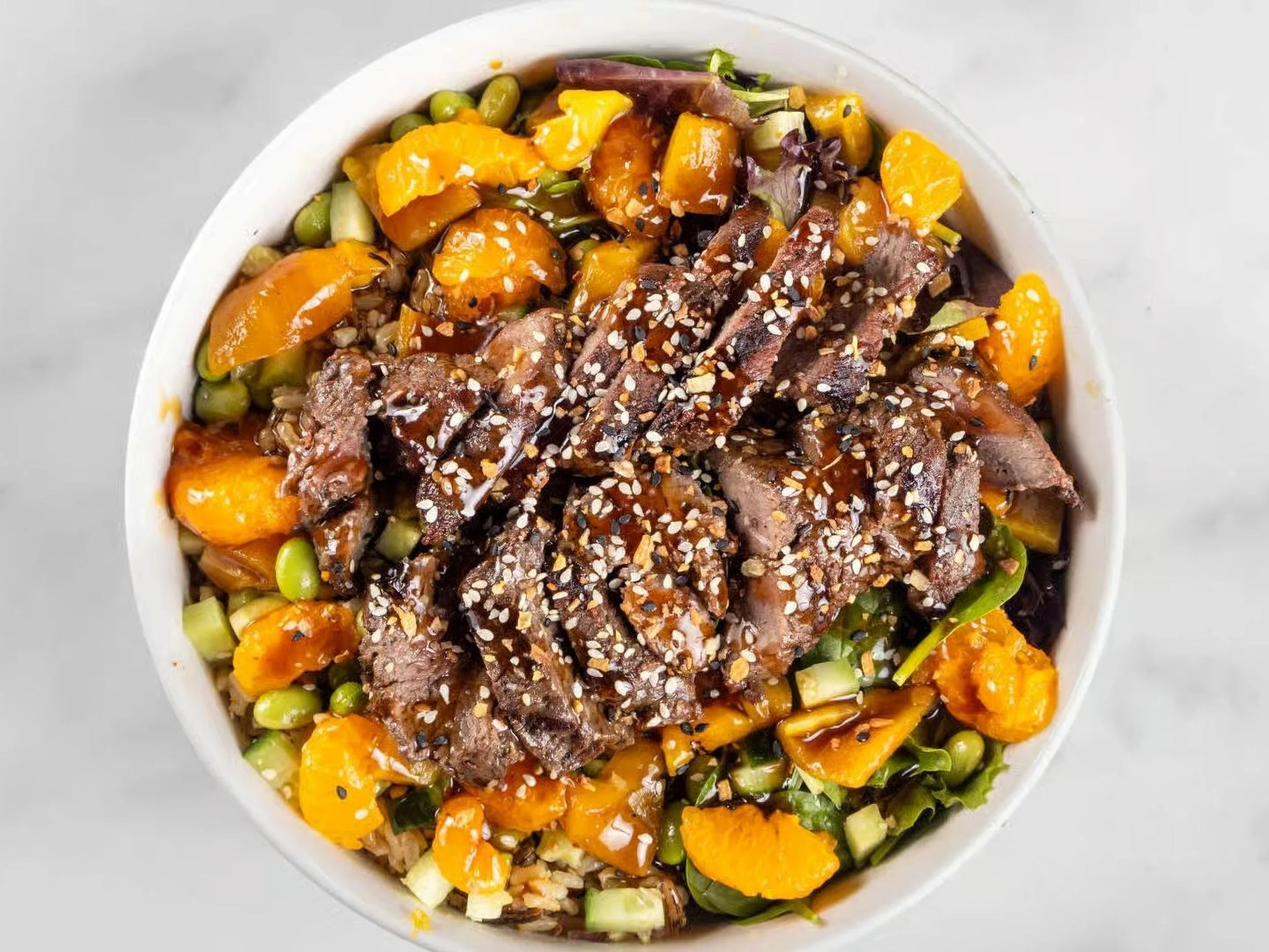 Bowl of rice topped with grilled meat, chopped vegetables, orange slices, and sesame seeds.