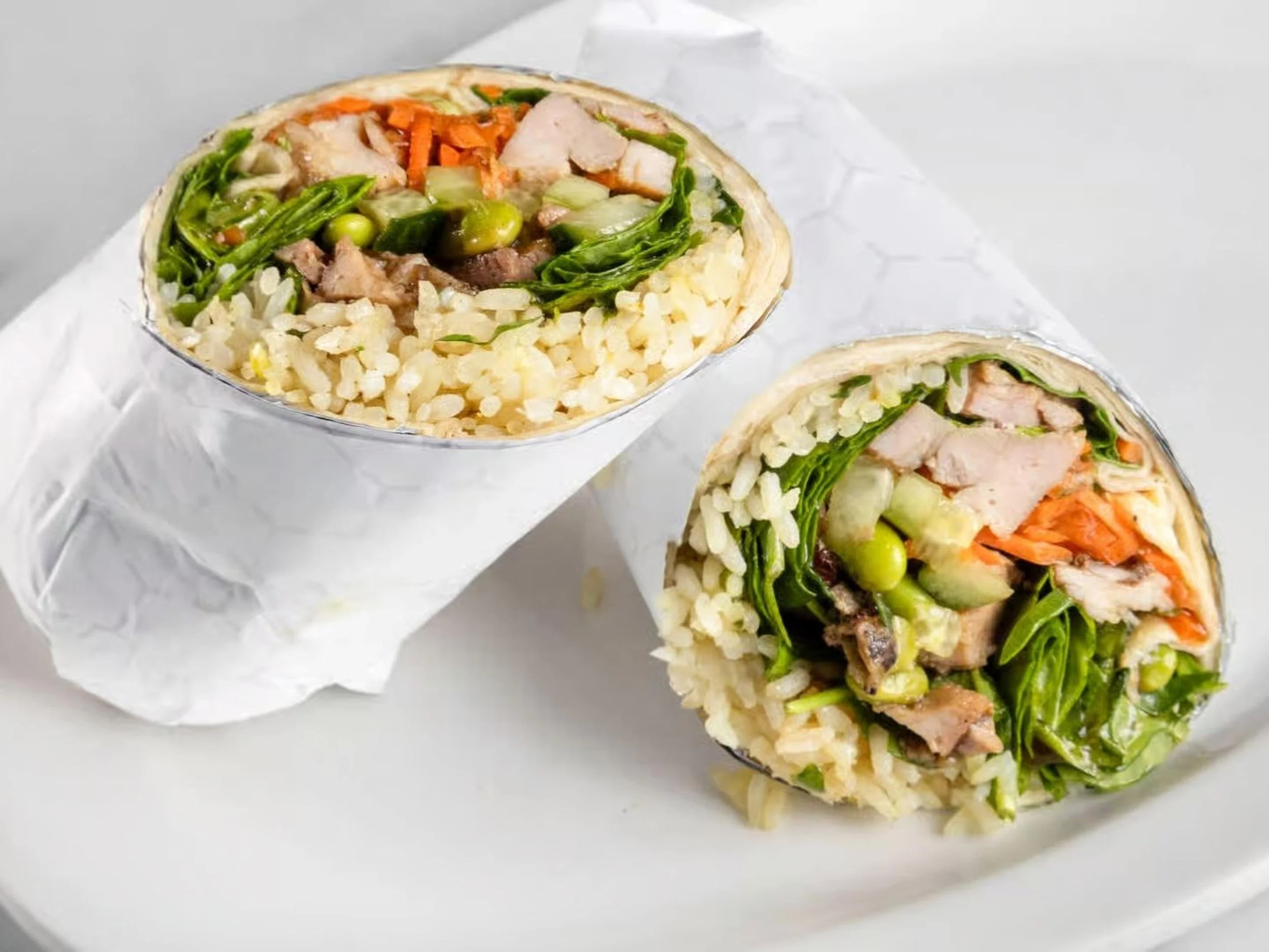Two rice paper wraps filled with vegetables and sliced chicken on a white plate.