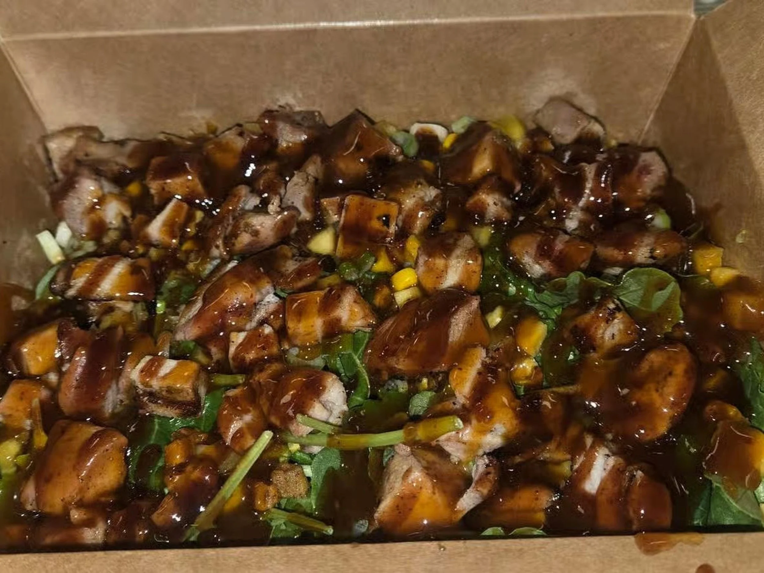 Chinese takeout box filled with chopped grilled chicken pieces topped with a dark sauce and garnish of chopped green onions.