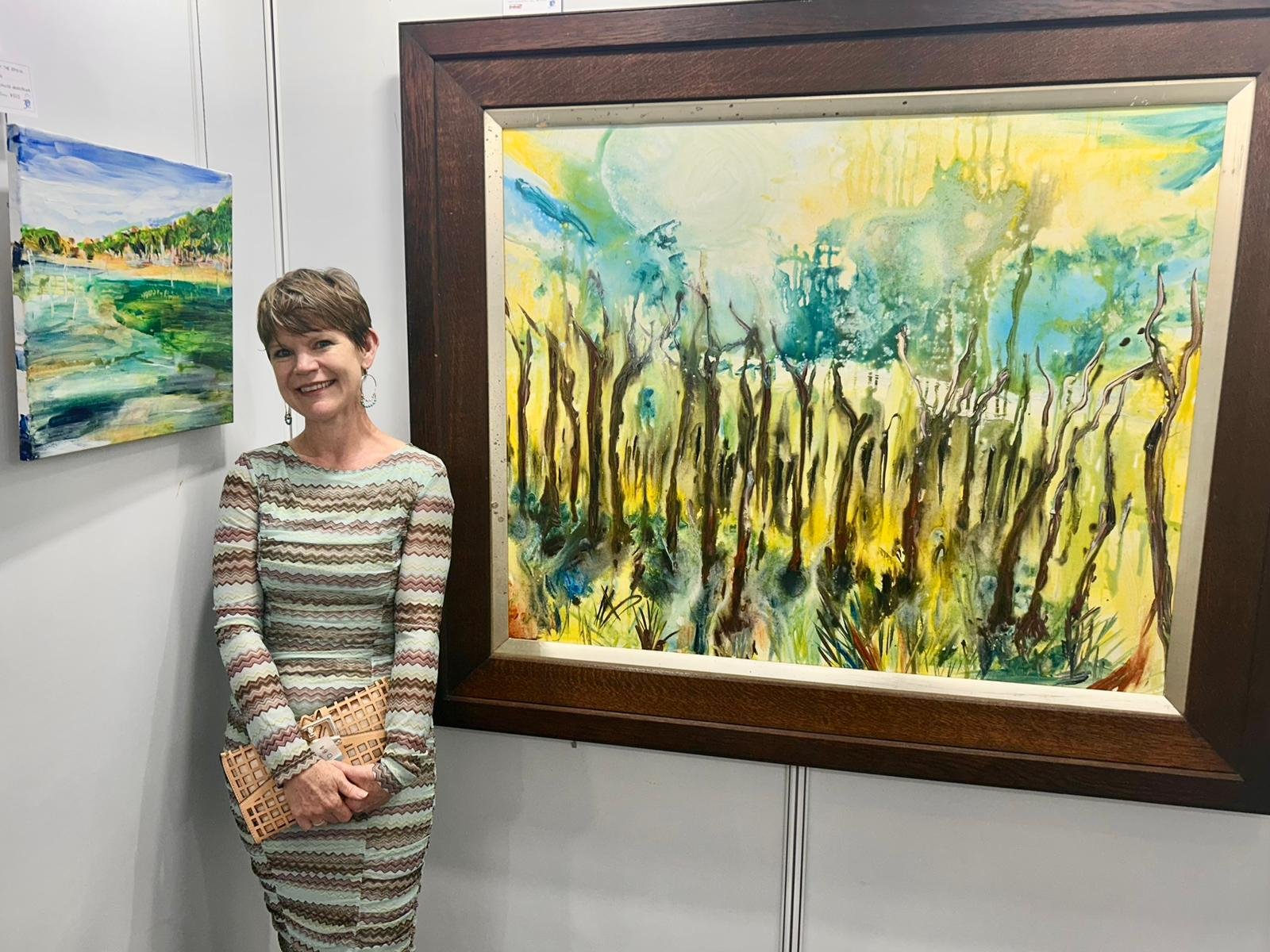 Artist Laura Kneebone, standing in front of a landscape painting at at art exhibition in Bundeena, Royal National Park, Sydney.