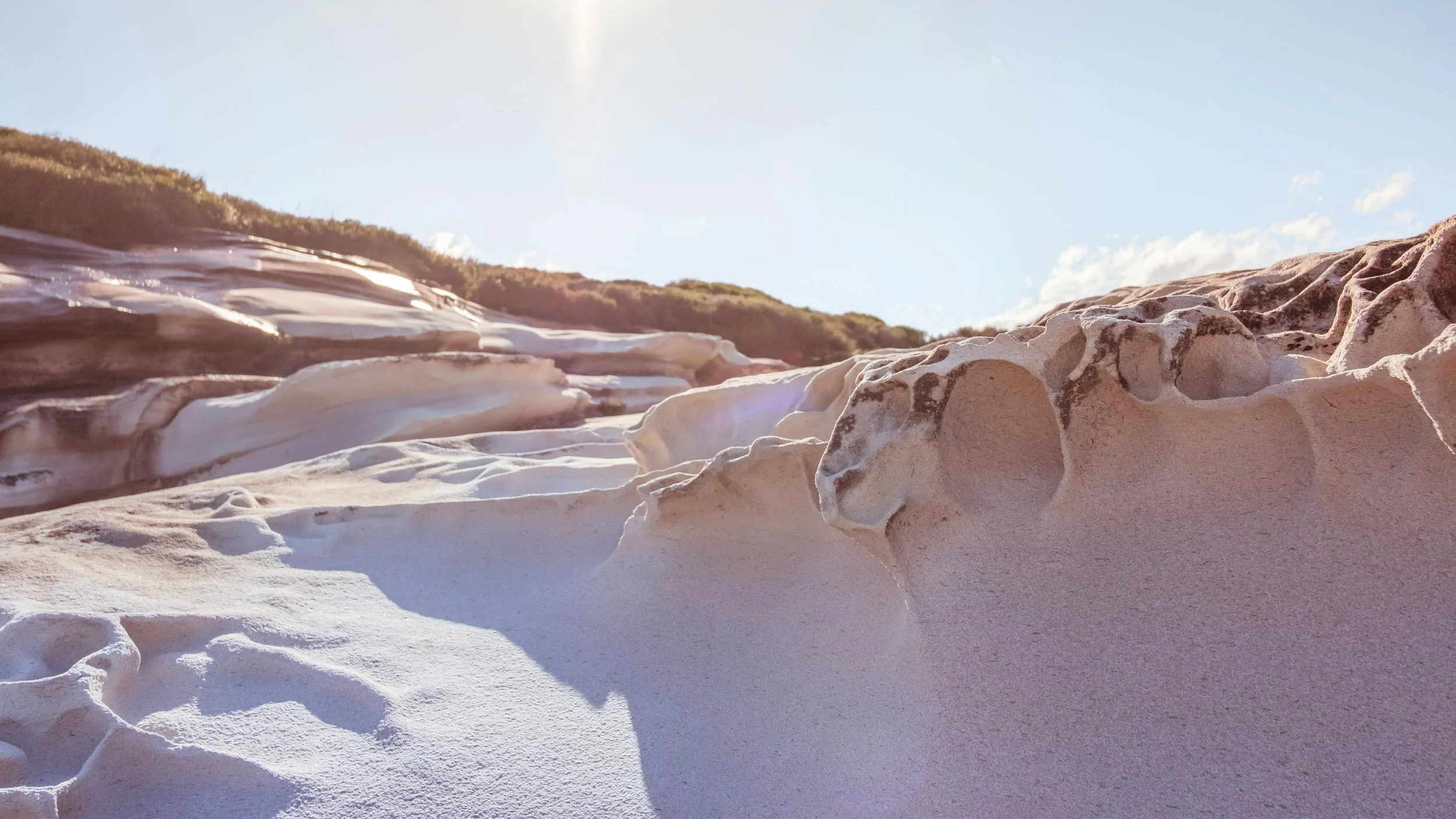 Close-up view of white and pinkish rocks on a beach with a blue sky and fluffy clouds in the background.