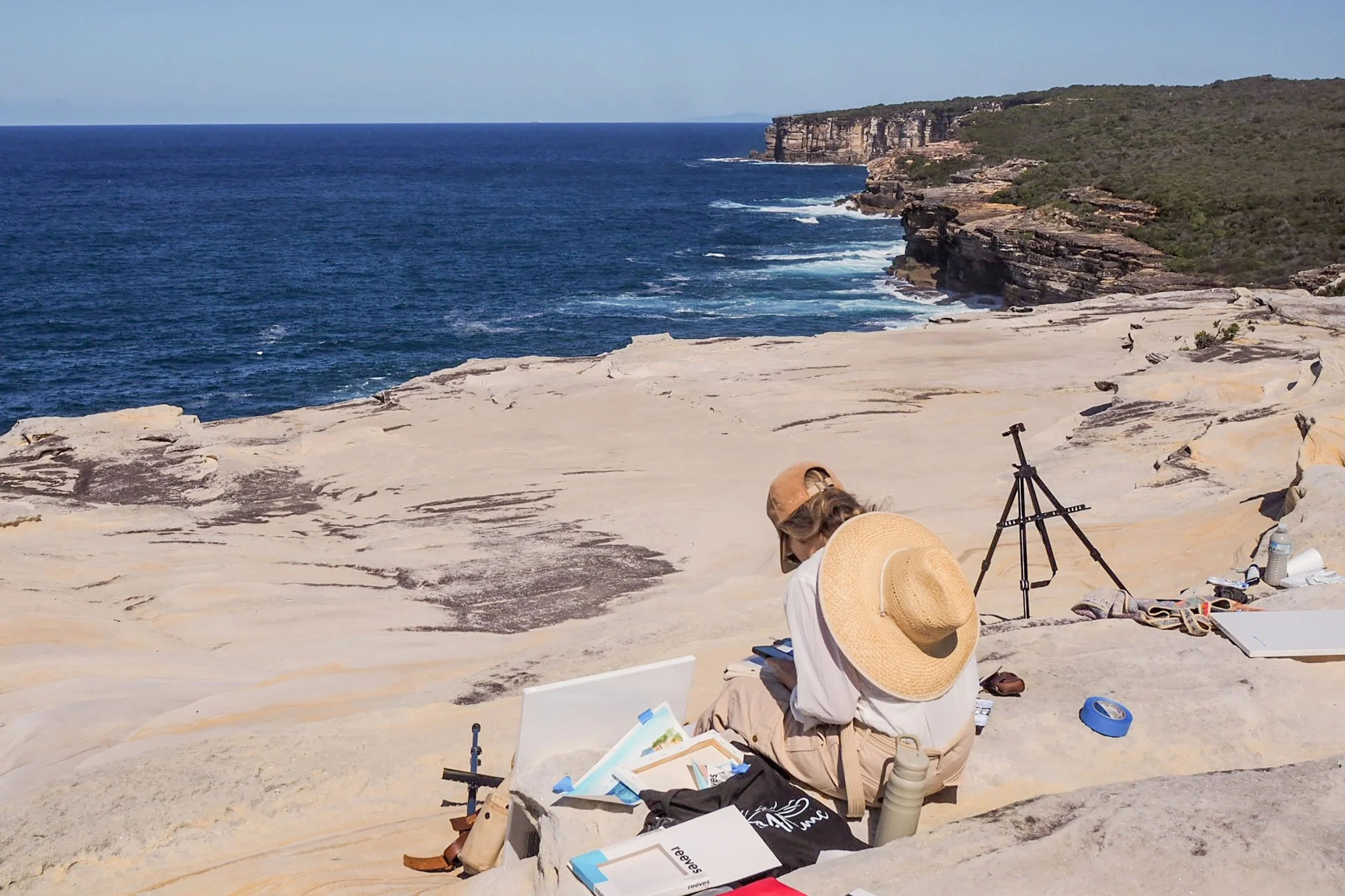 A woman in neutral clothes painting en plein air in a spectacular coastal location in Royal National Park, Sydney