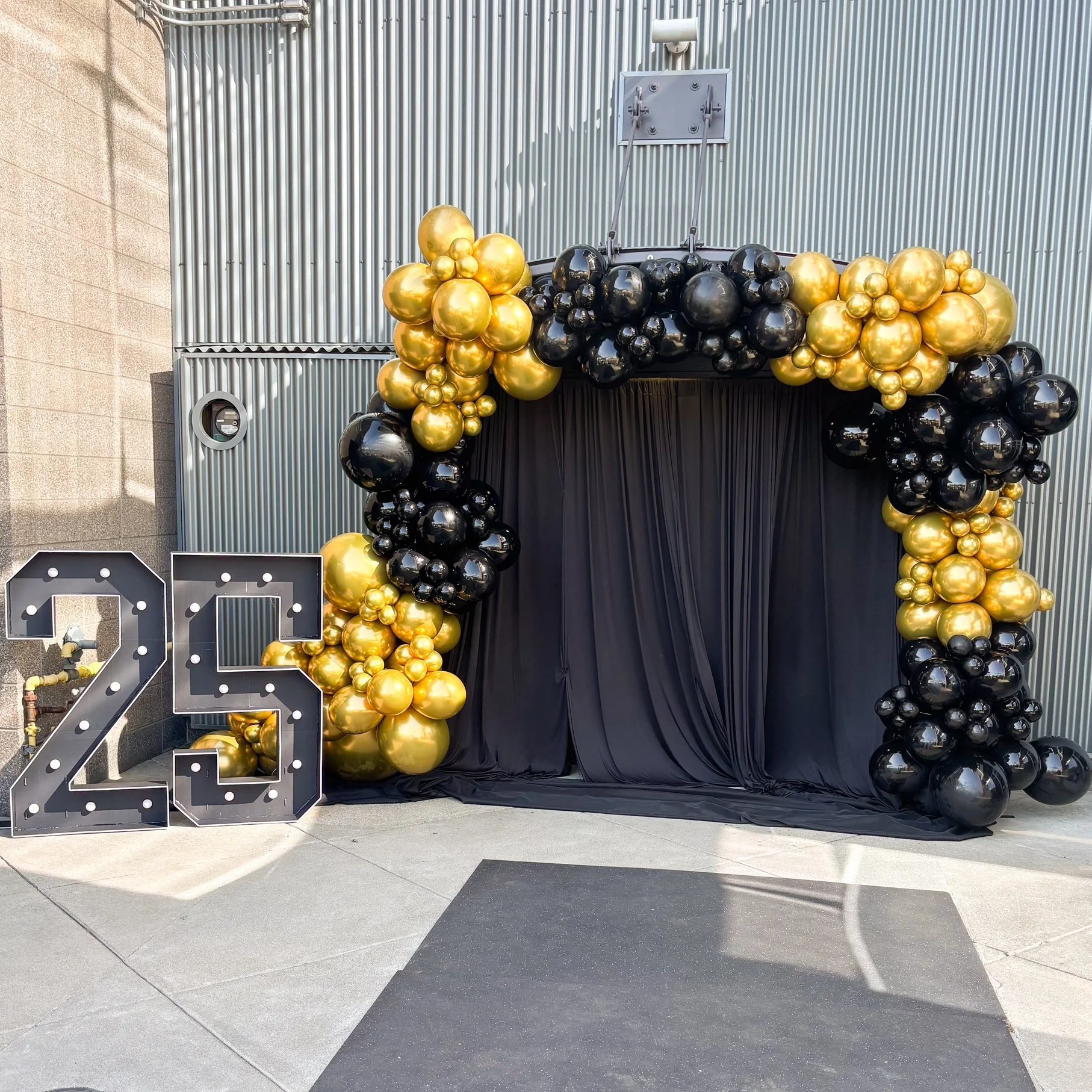 Decorative display with gold and black balloons arranged around a black curtain backdrop and large illuminated number 23.