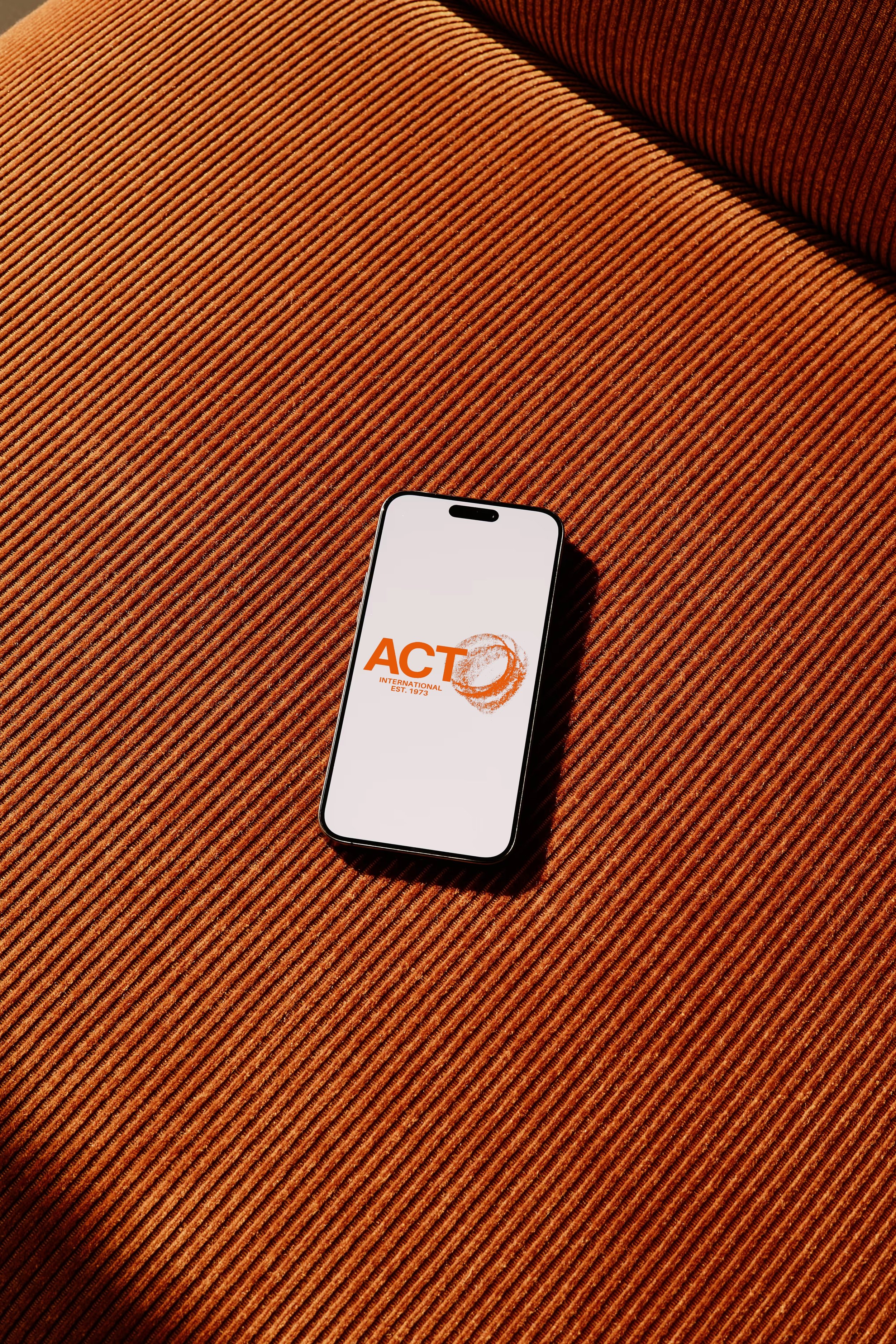 A smartphone with a white screen displaying the ACT logo on a textured orange cushion.