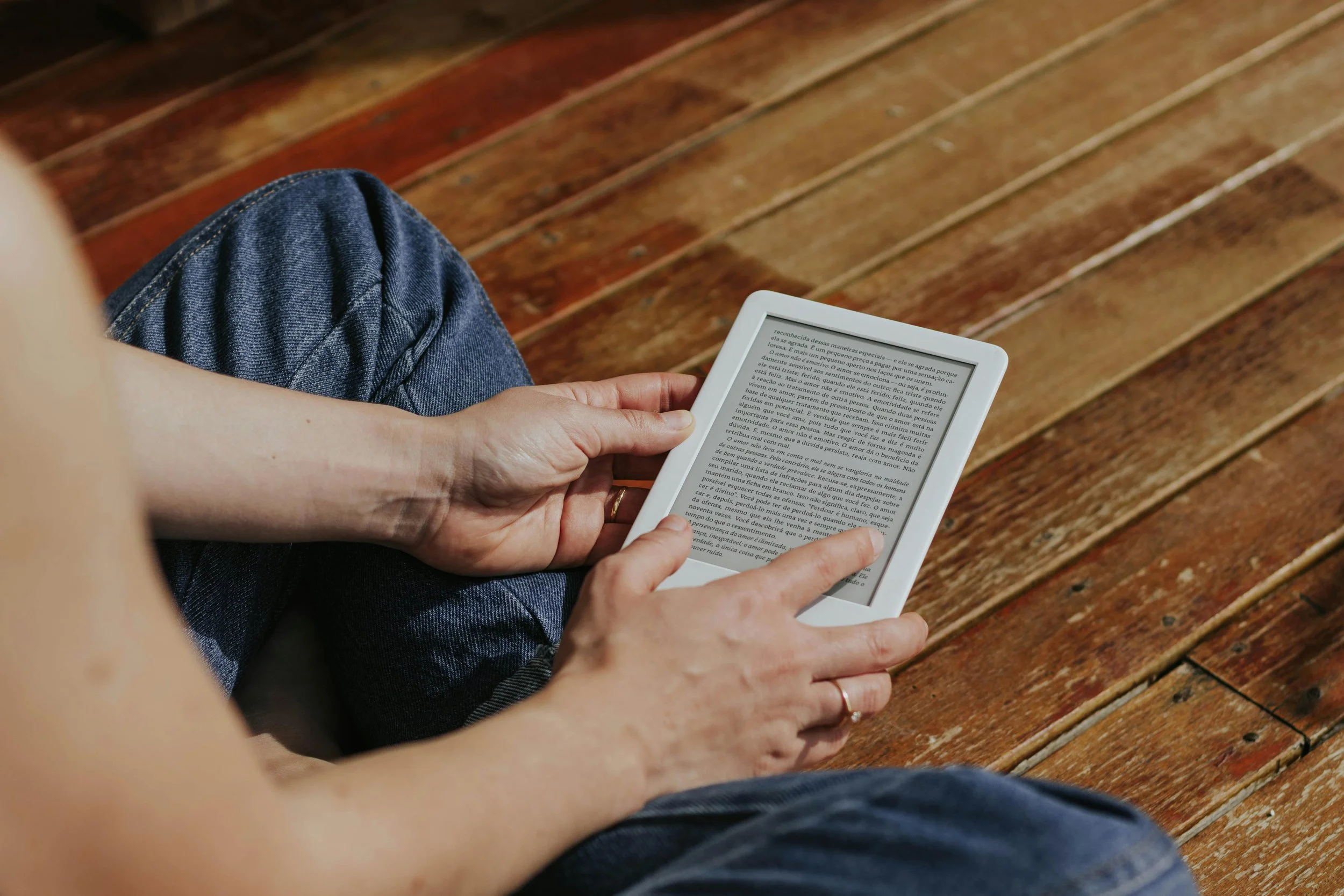 A person sitting on a wooden bench, holding an e-reader device with text on the screen.
