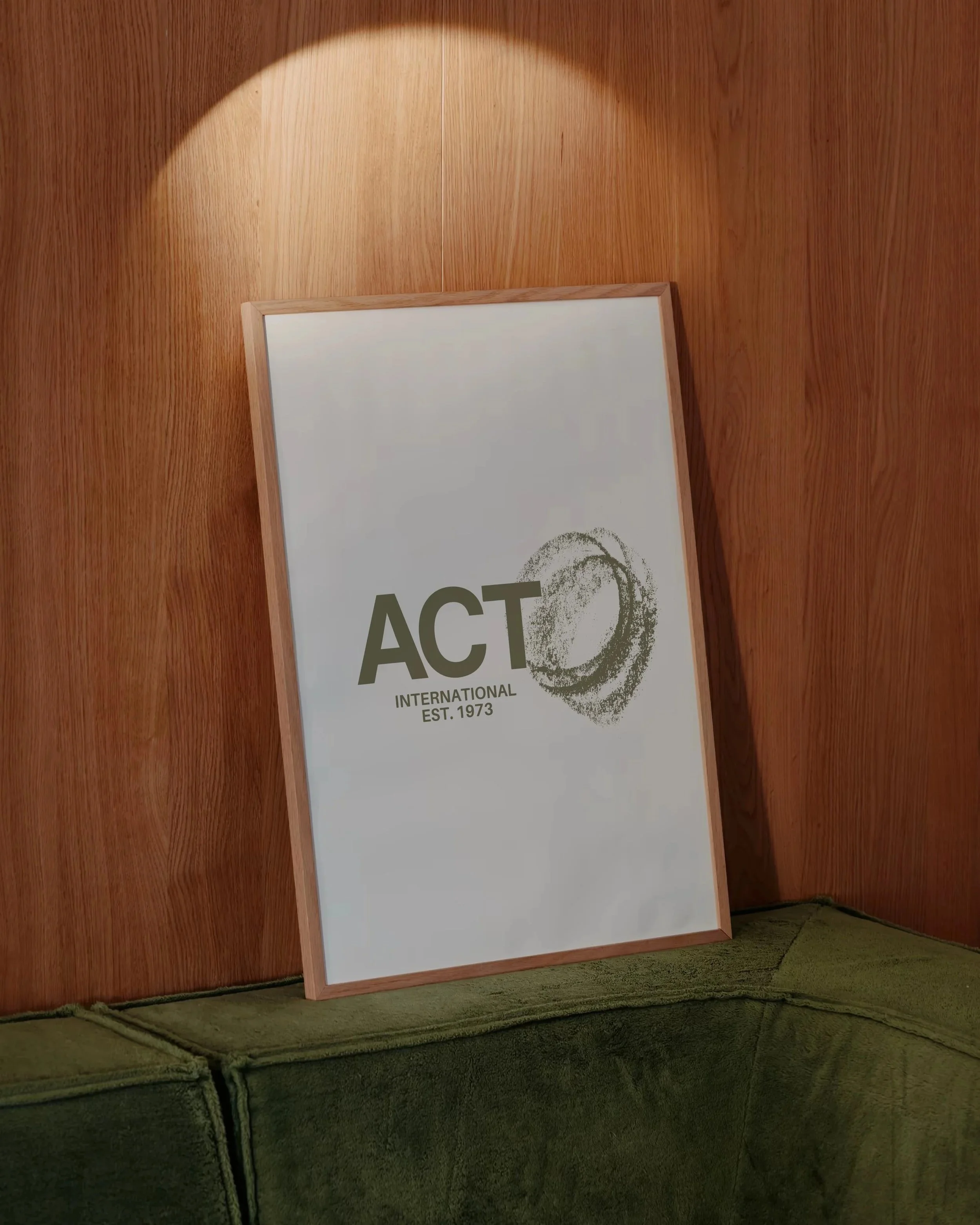 A framed poster with the word 'ACT' in large letters and an eye graphic, leaning against a wooden wall in a room with green carpeted floor.