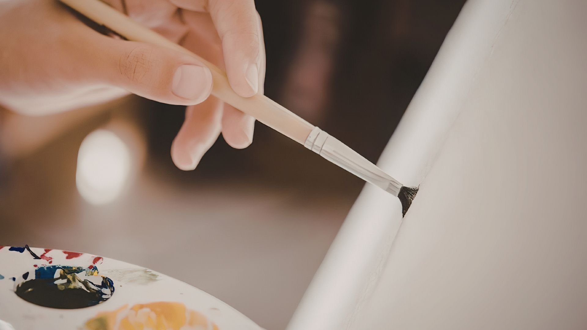 Close-up of a person painting a black line on a white canvas with a thin brush.