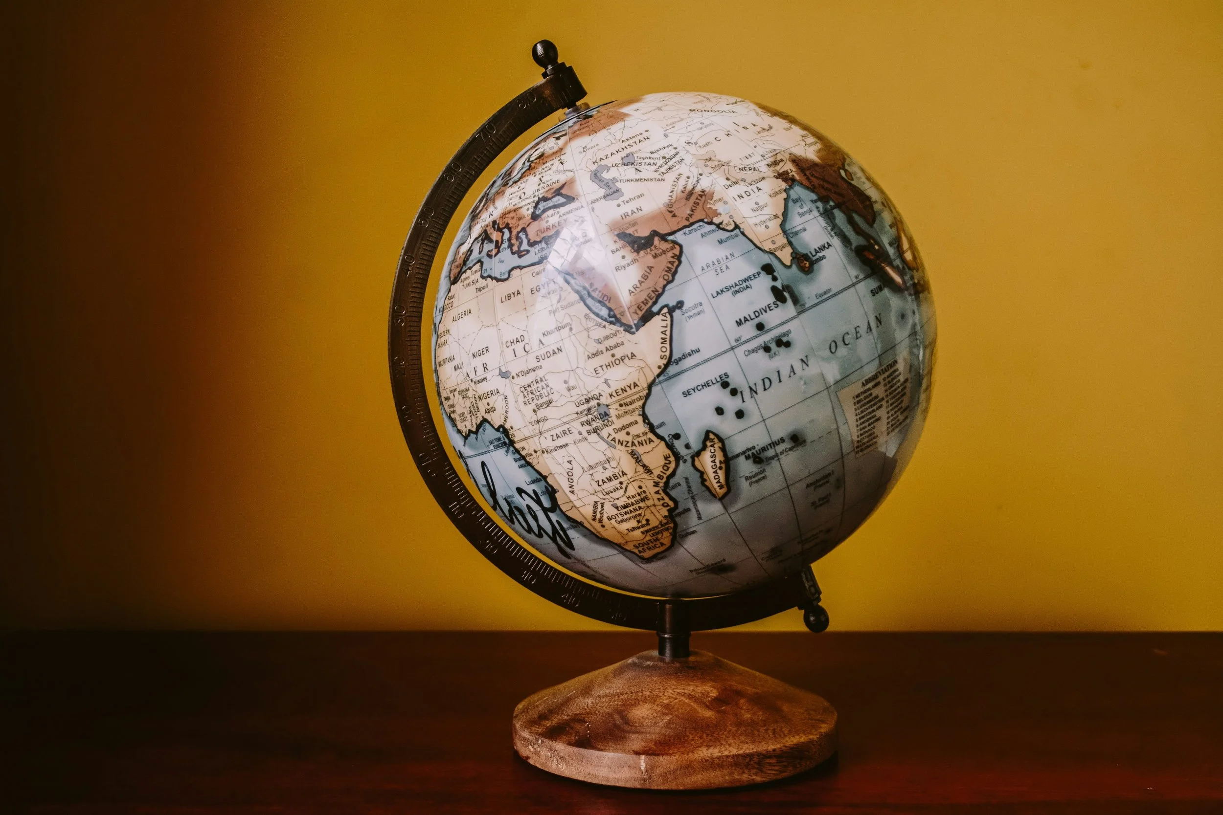 A globe on a wooden stand against a yellow background, showing parts of Europe, Africa, and Asia.