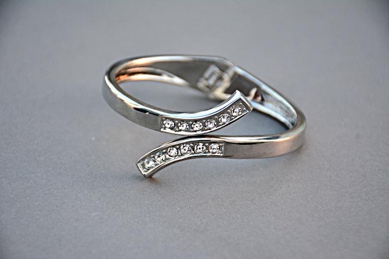 A silver ring with embedded clear stones in a curved and open design, placed on a gray surface.