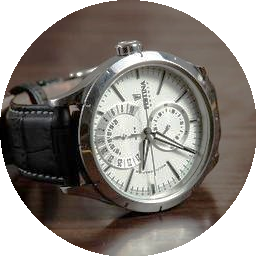 Silver wristwatch with a black leather strap on a wooden surface.